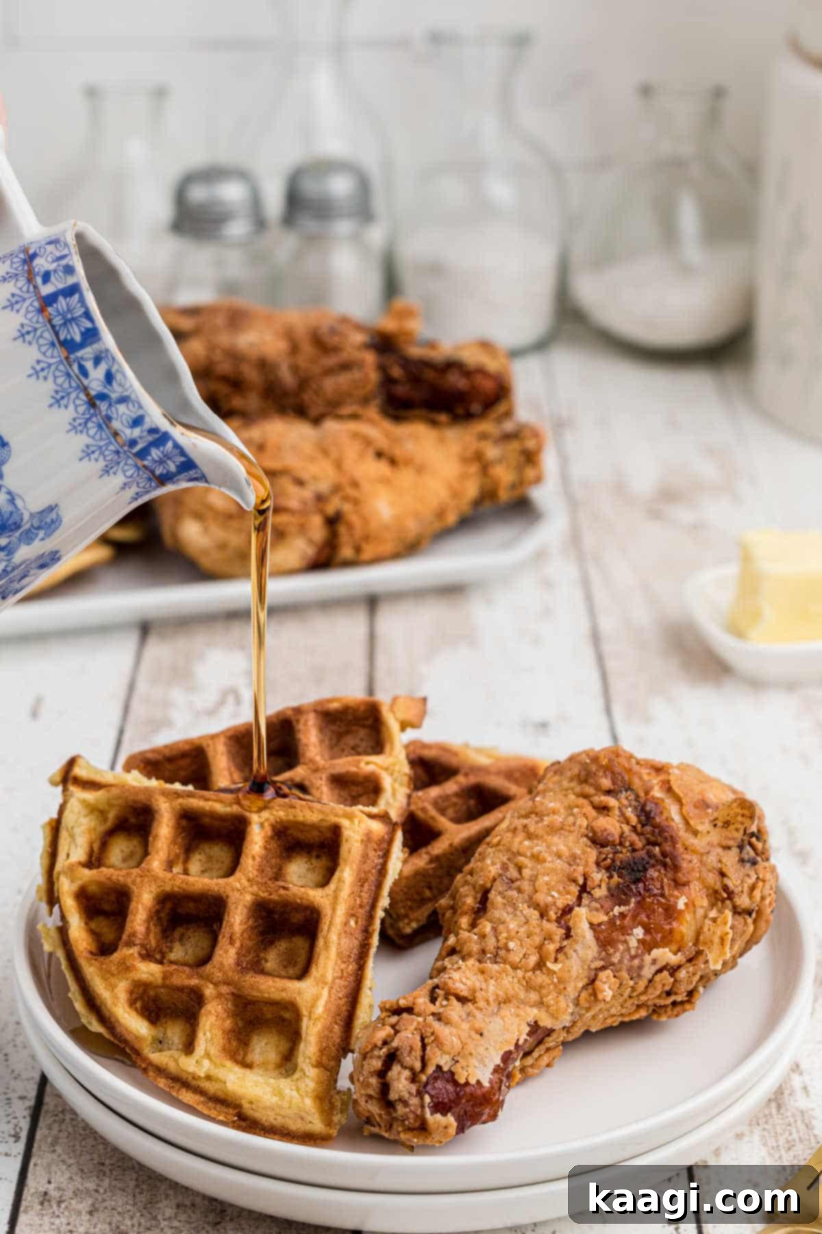 A plate with crispy fried chicken and golden waffles, with warm maple syrup being drizzled over the top.