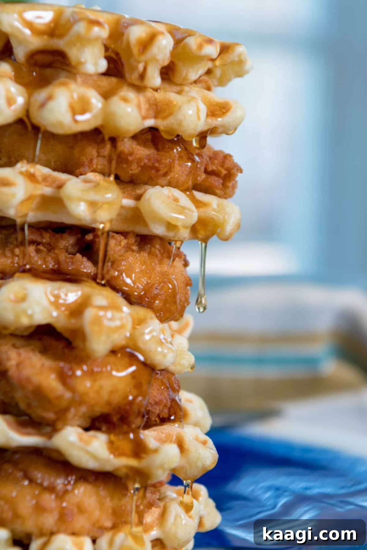 A stack of golden fried chicken pieces and fluffy waffles, with a generous drizzle of syrup cascading down the sides.