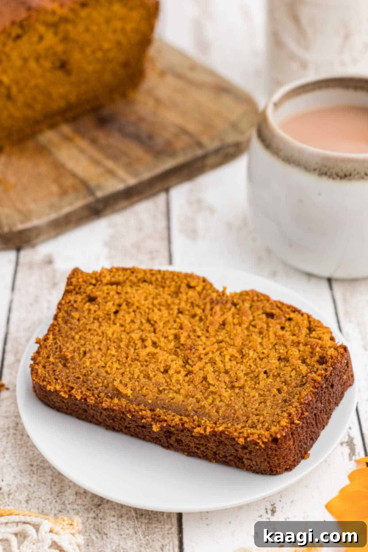 A perfect slice of Amish Pumpkin Bread resting on a white plate, with a steaming cup of coffee blurred in the background, ready for a cozy moment.