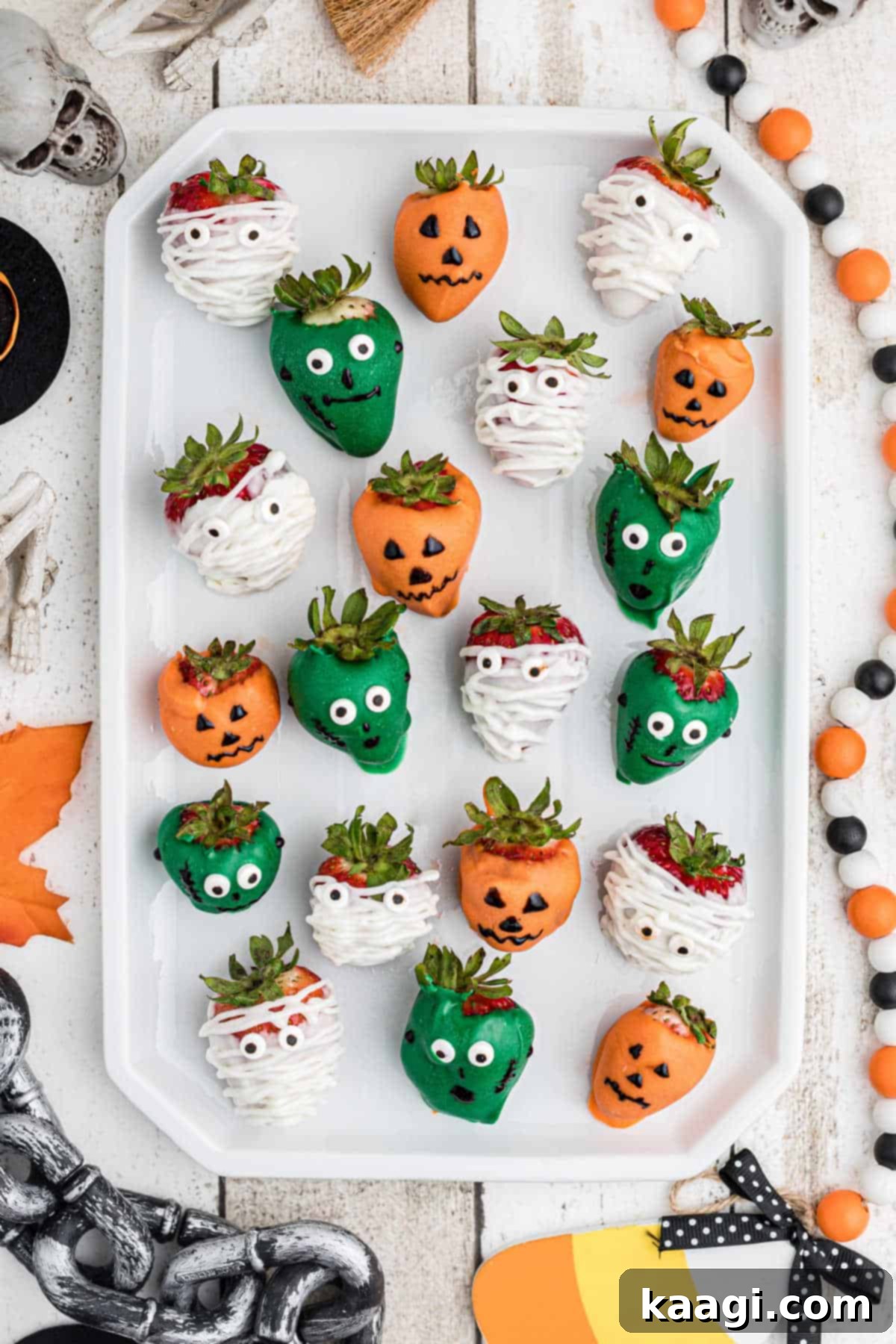 Overhead shot of a plate of Halloween chocolate covered strawberries, featuring mummy, Frankenstein, and Jack-o'-lantern designs.