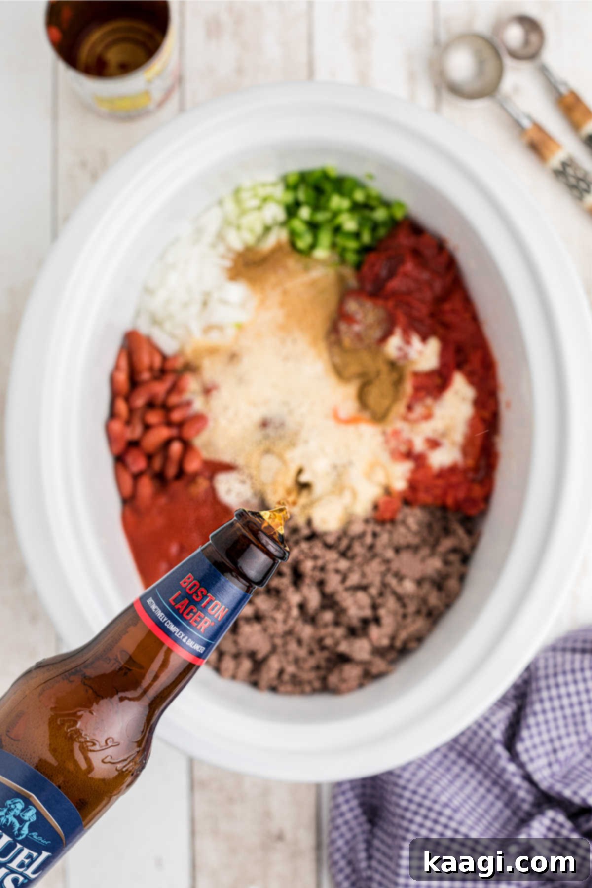 Pouring a bottle of beer directly into the slow cooker, filled with chili ingredients.