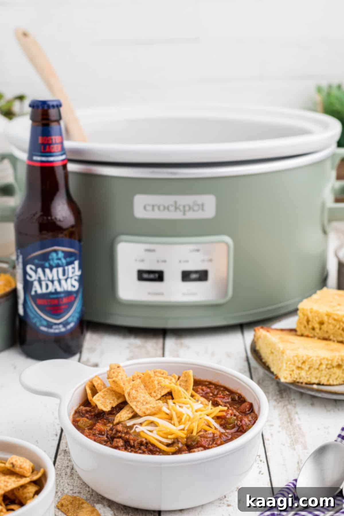 A beautifully presented bowl of beer chili, garnished and ready to eat, with a crock pot and a bottle of beer blurred in the background.