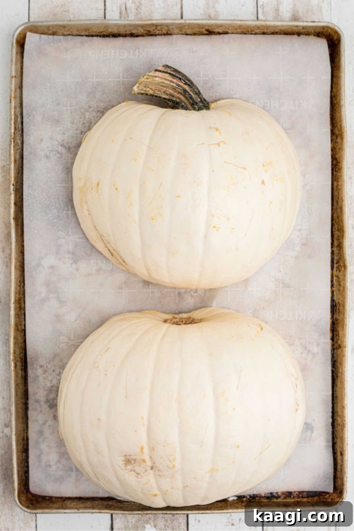 Two white pumpkin halves, face down on a baking sheet, ready to be baked.