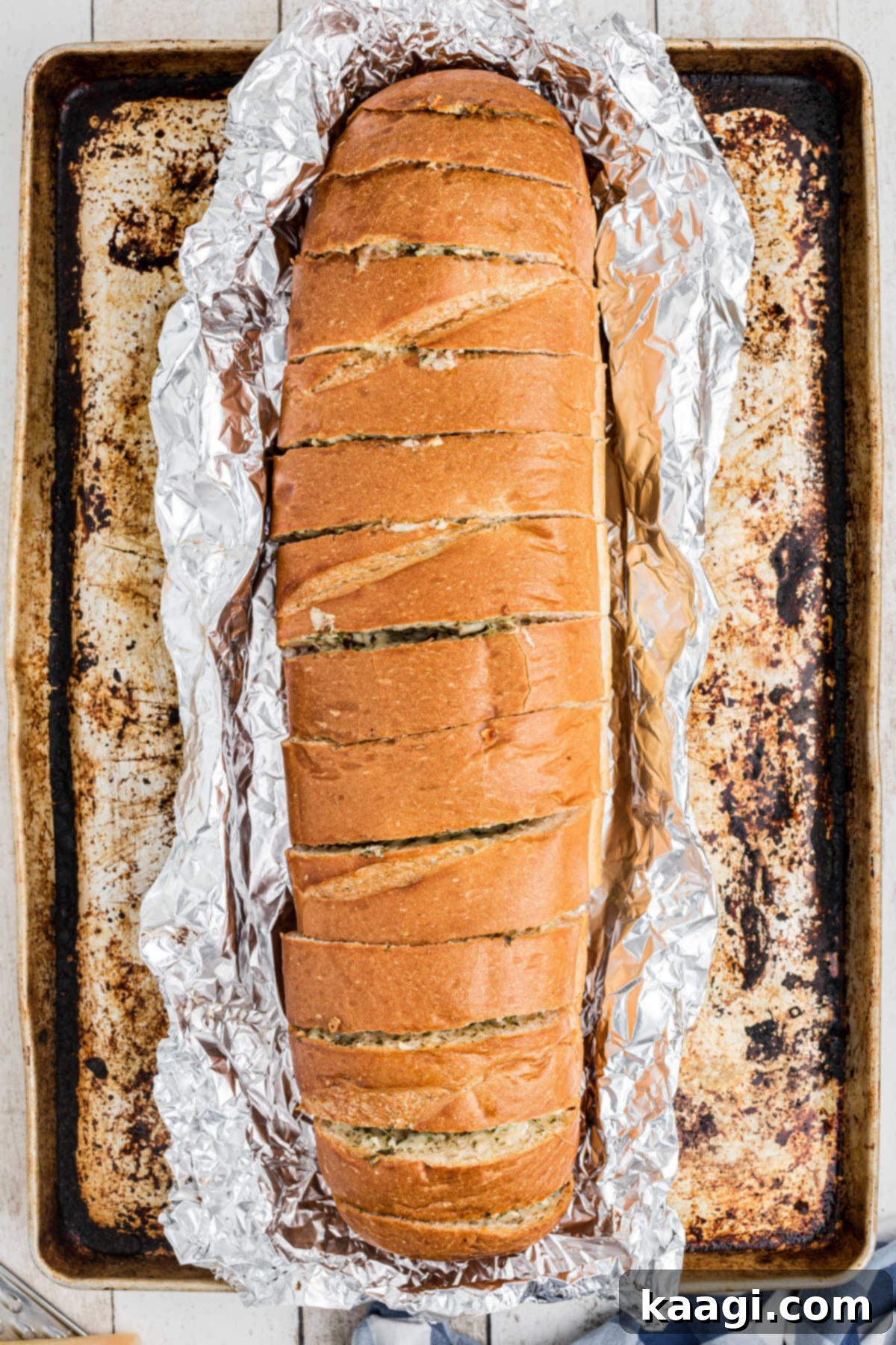 A baking sheet with a loaf of stuffed garlic bread still in foil, fresh out of the oven.