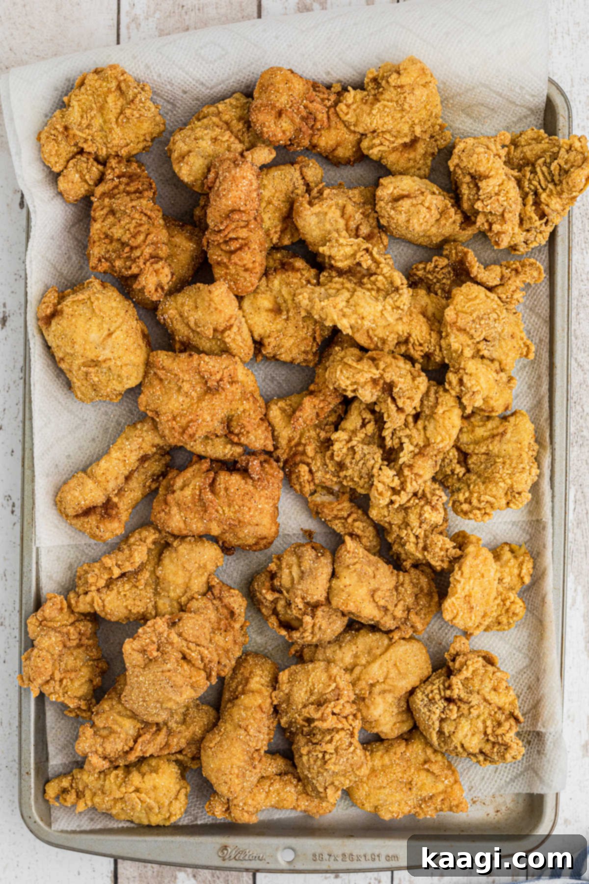 Overhead shot of a full baking sheet of golden, crispy fried fish, garnished with lemon wedges, ready to serve.
