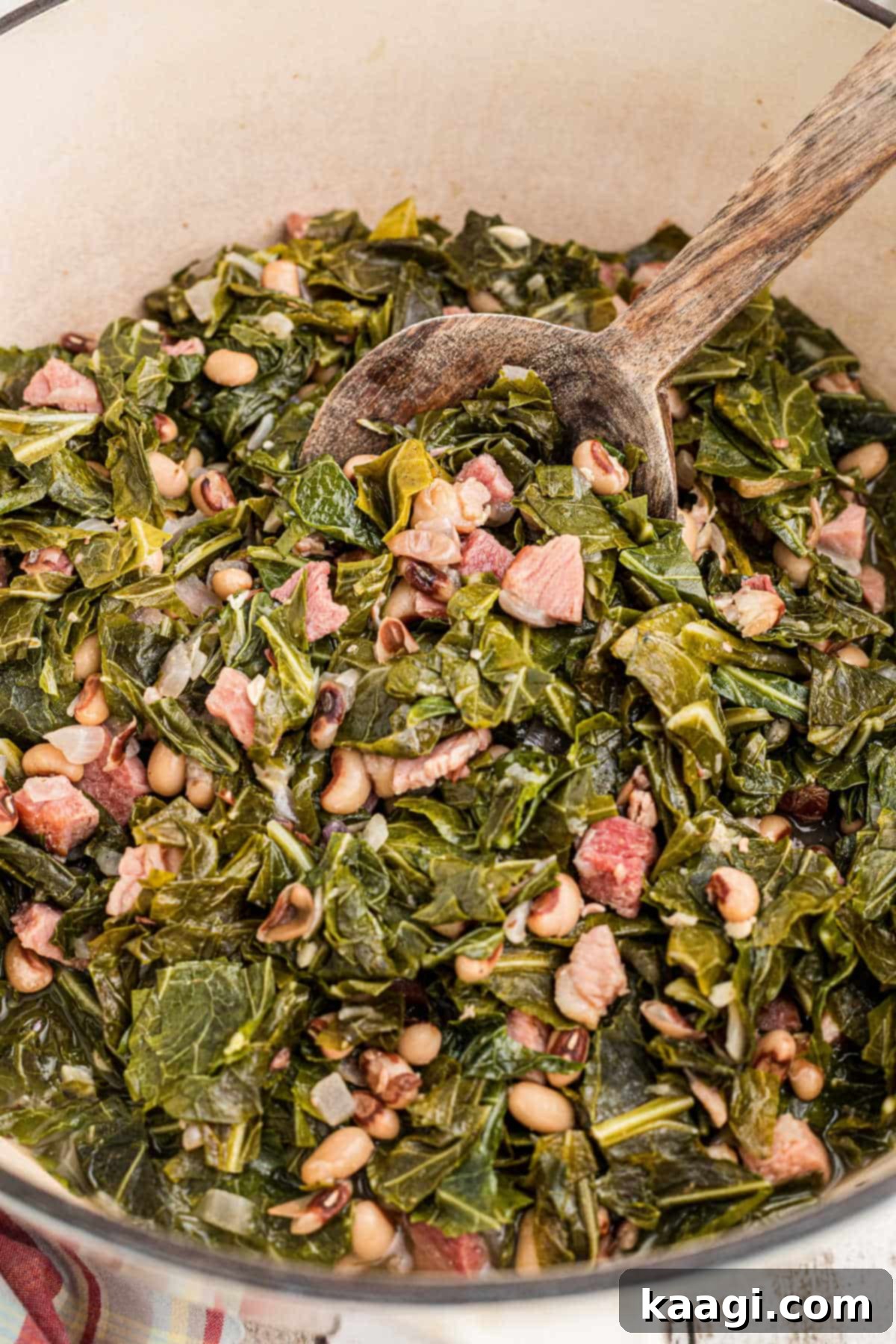 Closeup inside a pot with a spoon digging into the collard greens and black eyed peas, showing the rich, dark liquid.
