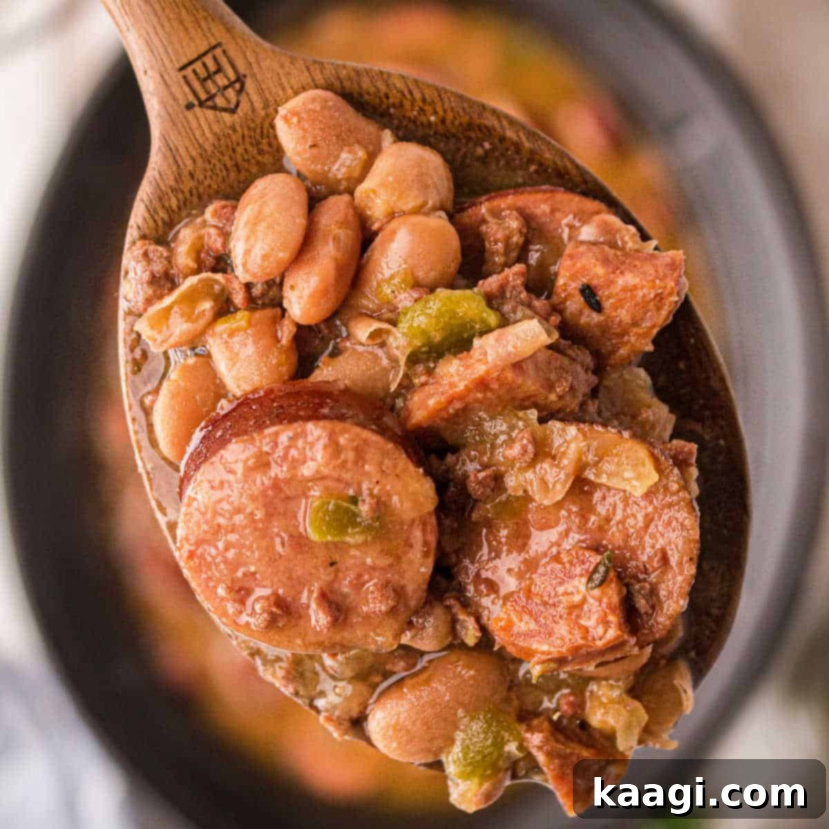 Close up of some pinto beans and sausage on a spoon over a crock pot.