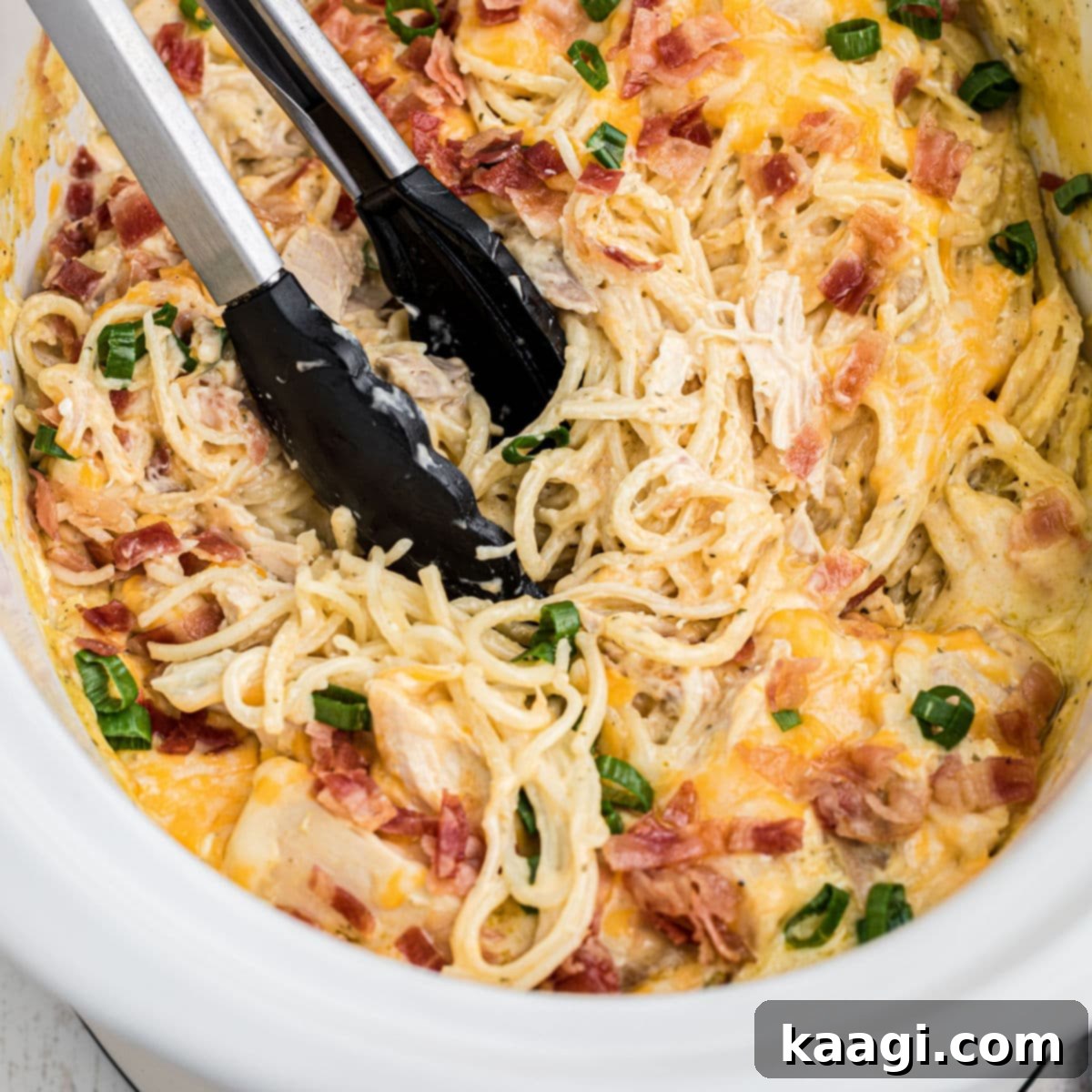 A pair of tongs digging into a crock pot ranch chicken spaghetti.