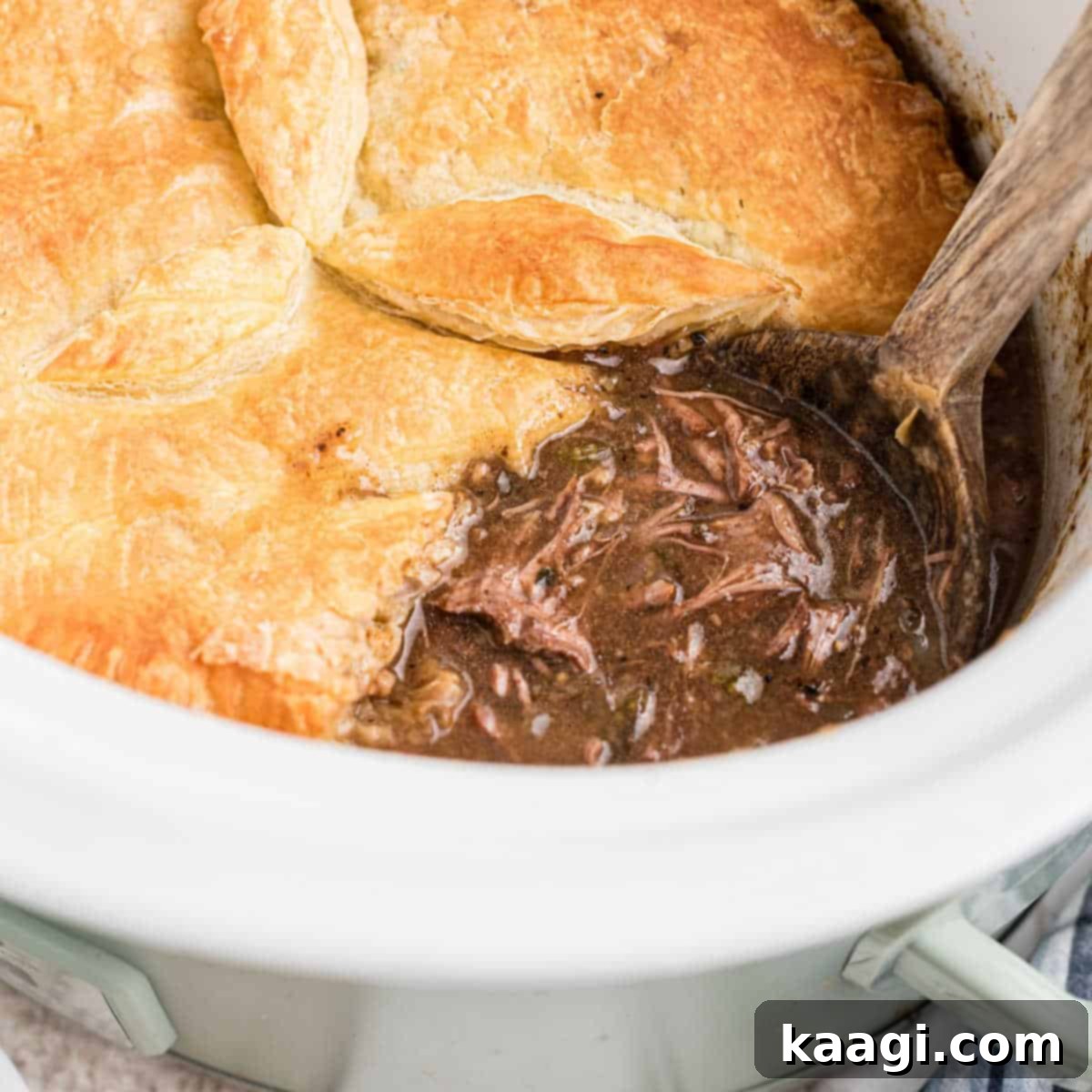 Slow cooker steak pie with a wooden spoon sitting in it.