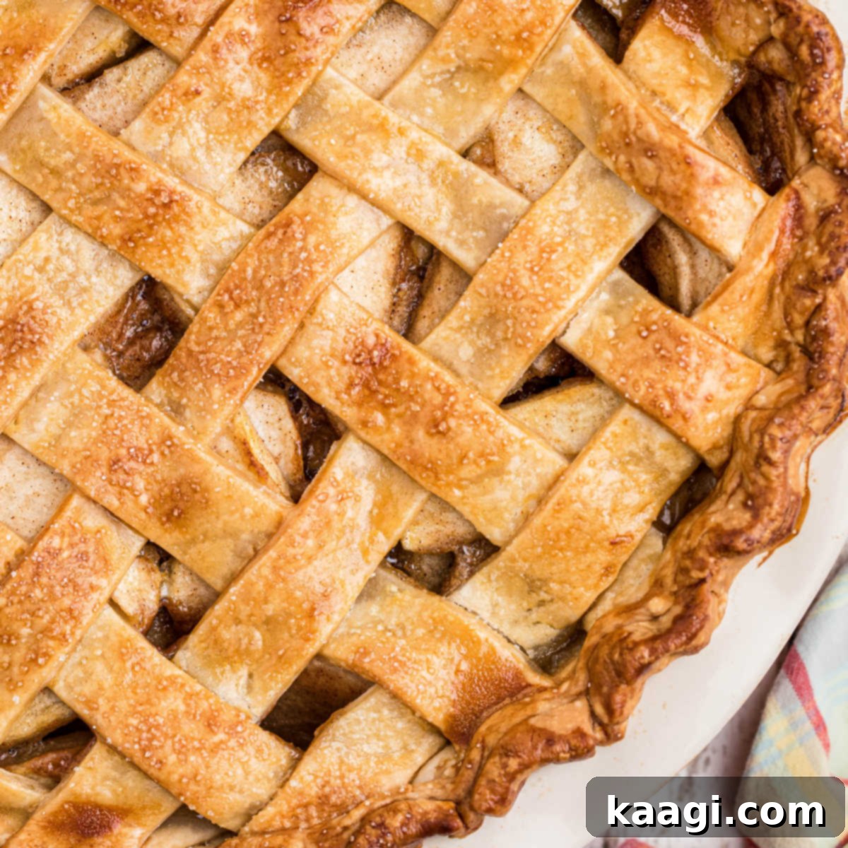 Close-up view of the golden, beautifully baked, and flaky crust of a classic country apple pie, revealing hints of cinnamon and baked apple filling peeking through.