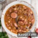 Overhead shot of a bowl of Cajun 15 bean soup with a spoon digging in, showing the rich, thick texture.
