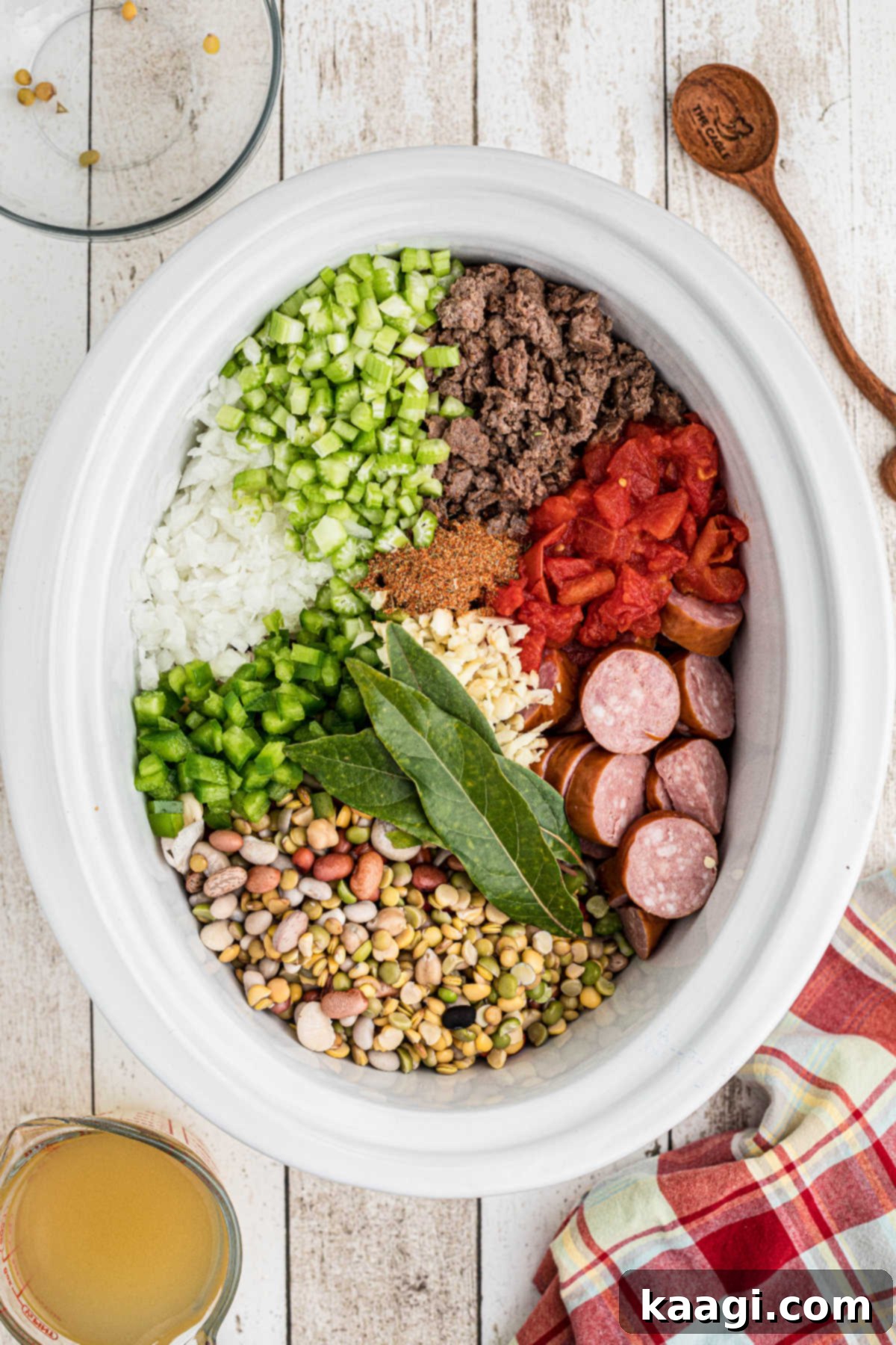 Slow cooker filled with pre-soaked beans, browned ground meat, and chopped vegetables, ready for cooking.