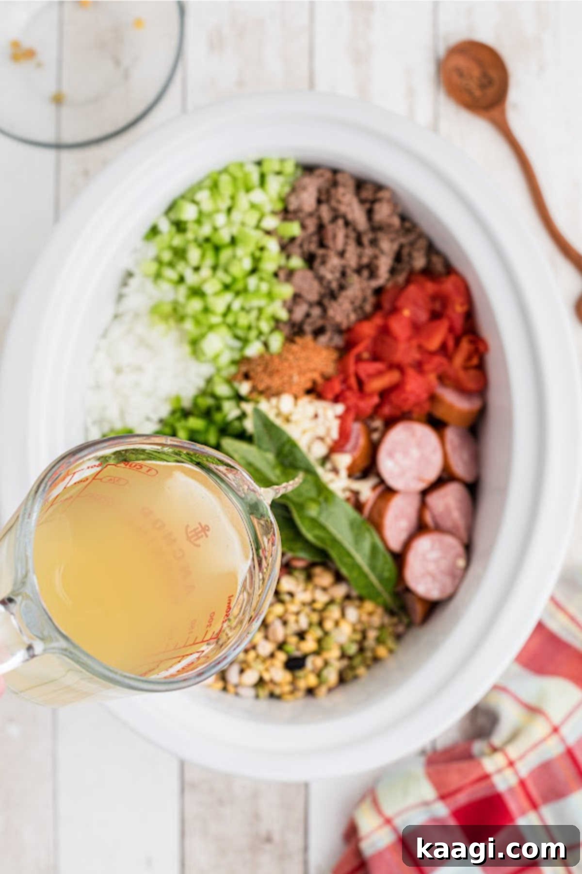 Chicken broth being poured into a slow cooker filled with all the Cajun 15 bean soup ingredients.