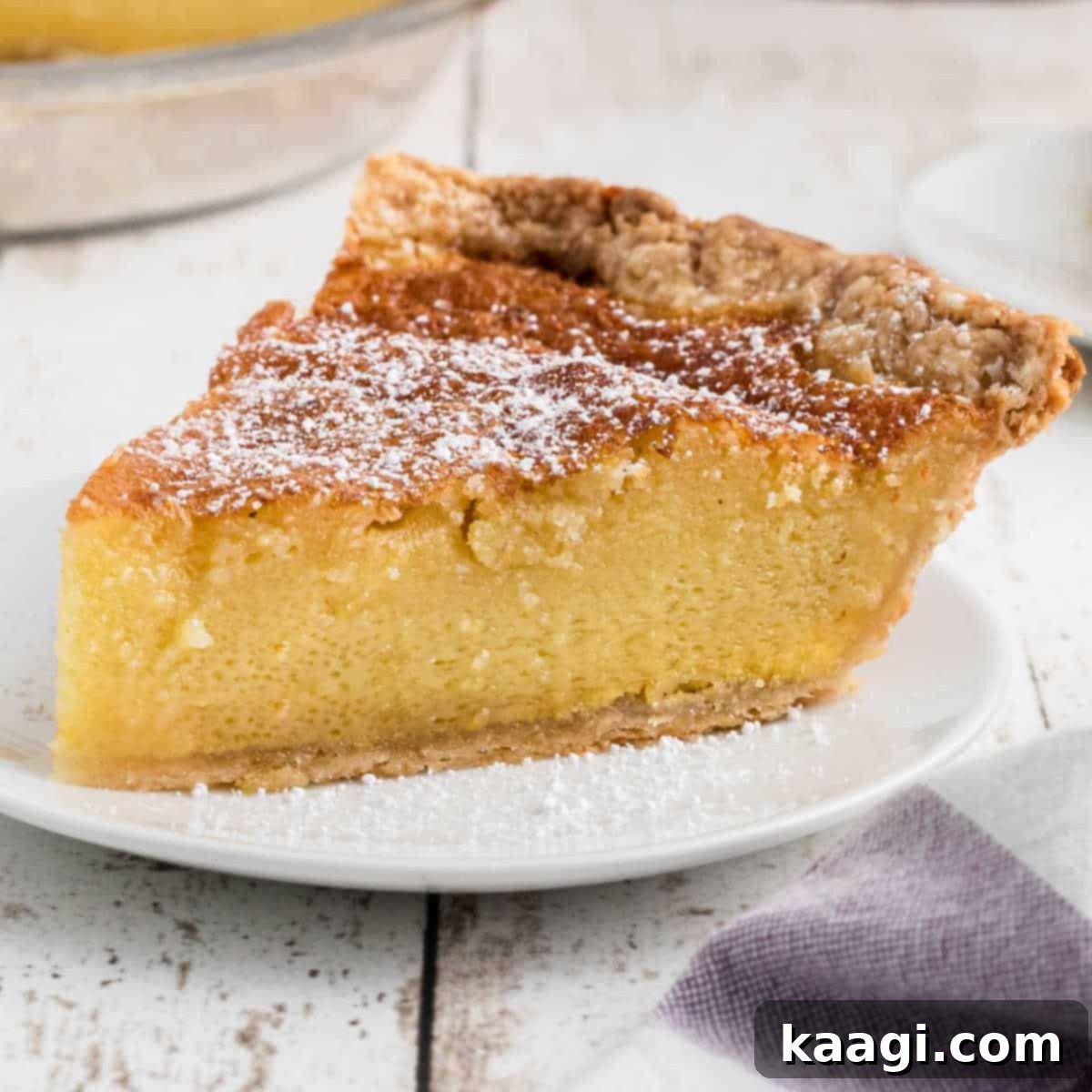 A slice of old fashioned chess pie with a dusting of powdered sugar, cropped square, indicating its sweet and rustic charm.