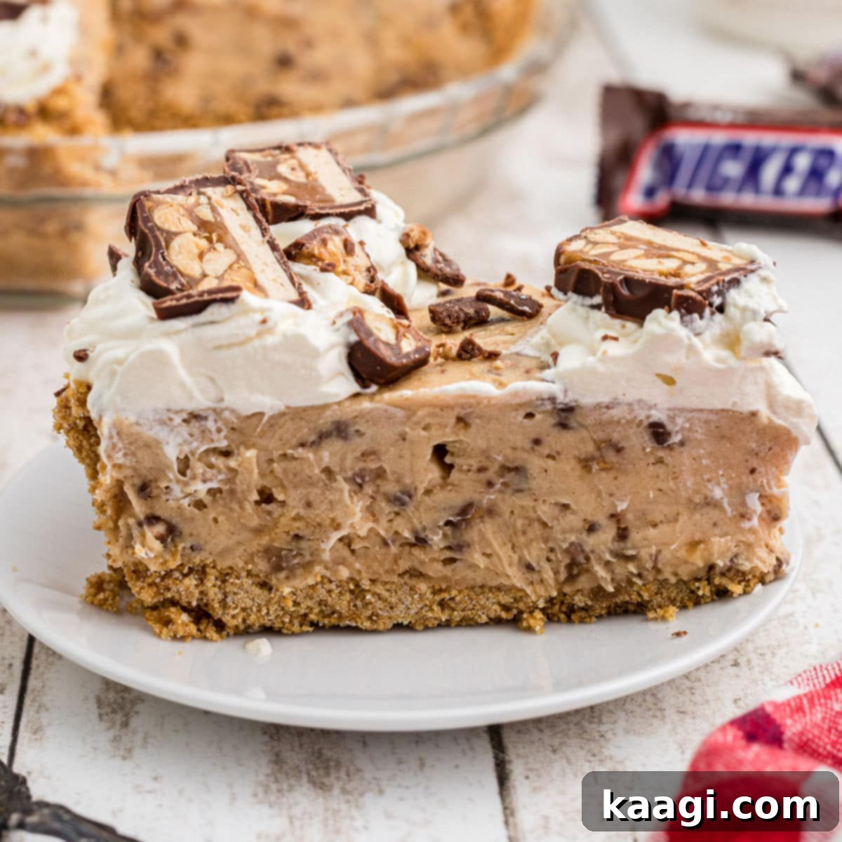 A close up of a slice of no bake snickers pie, showing its layers of chocolate, caramel, and peanuts.
