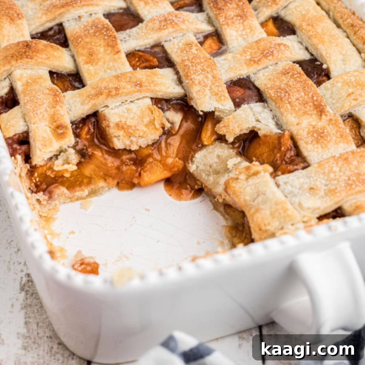Dish with a Southern peach cobbler featuring a golden pie crust, some portions scooped out, cropped square.