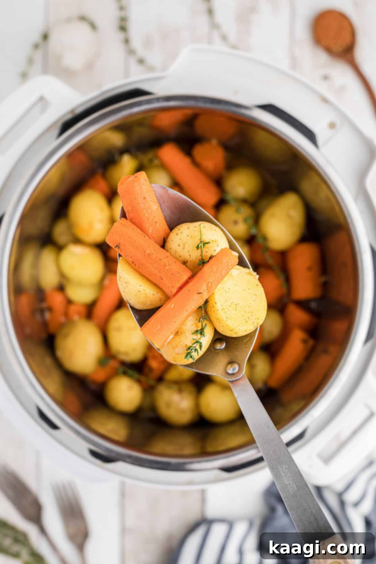 Overhead shot of an Instant Pot filled with perfectly cooked potatoes and carrots, with a serving spoon poised to dish out a portion.