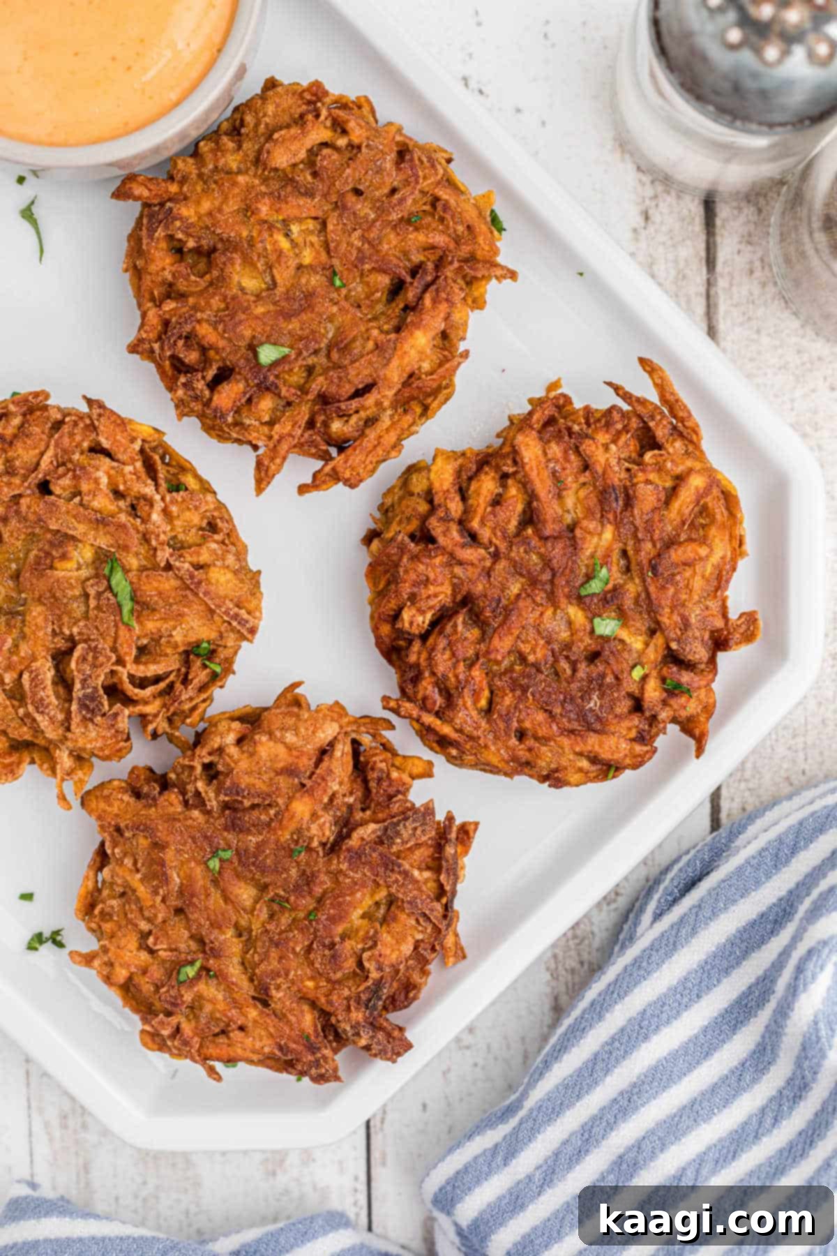 Overhead shot of a plate of beautifully golden and crispy sweet potato fritters, garnished with fresh herbs and served alongside a small bowl of creamy sweet and spicy dip.