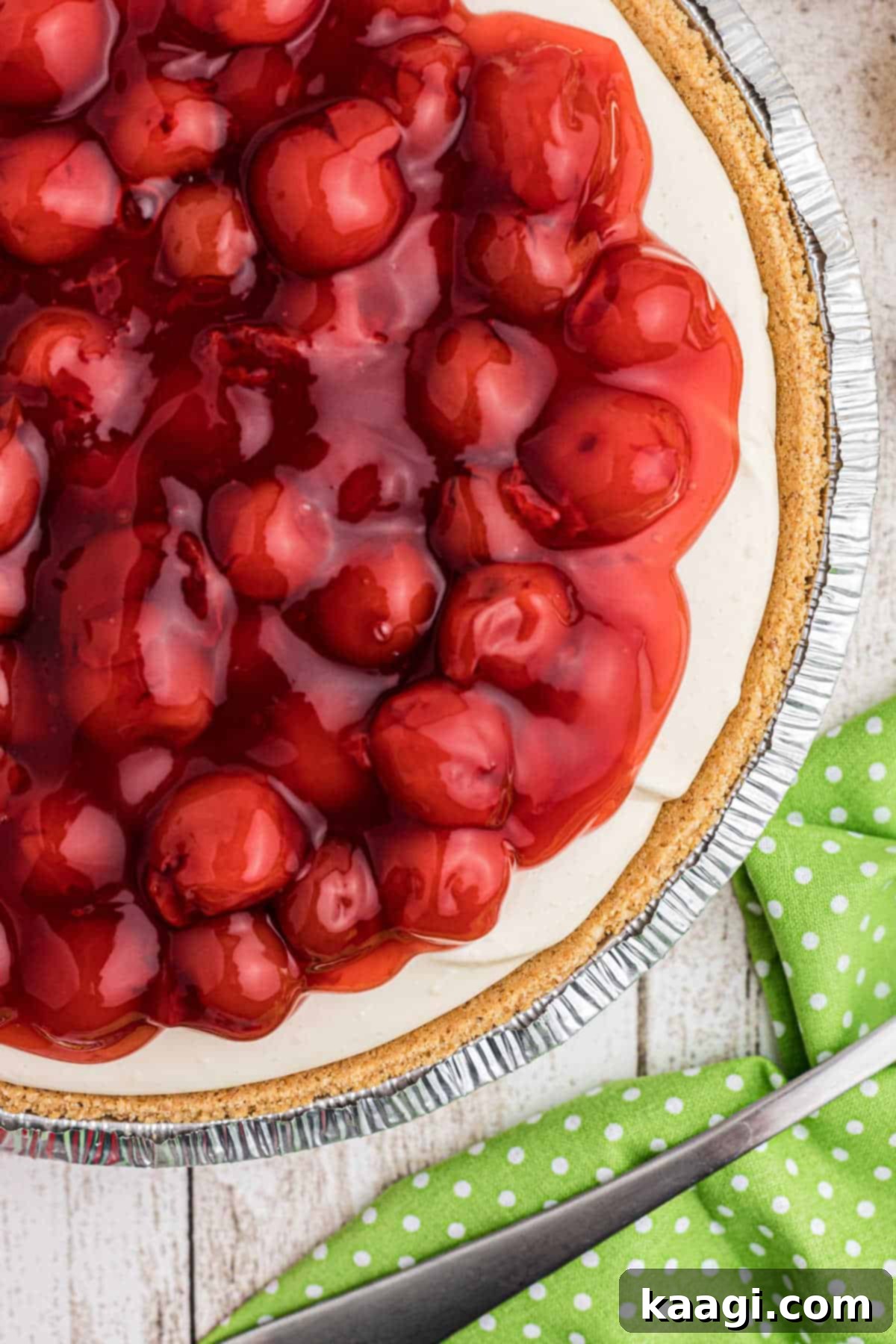 Close-up side shot of a perfectly set no-bake cherry pie, showcasing its creamy filling and vibrant fruit topping against a golden graham cracker crust.
