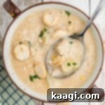 A cropped square image of a bowl of crab chowder with a spoon digging in.