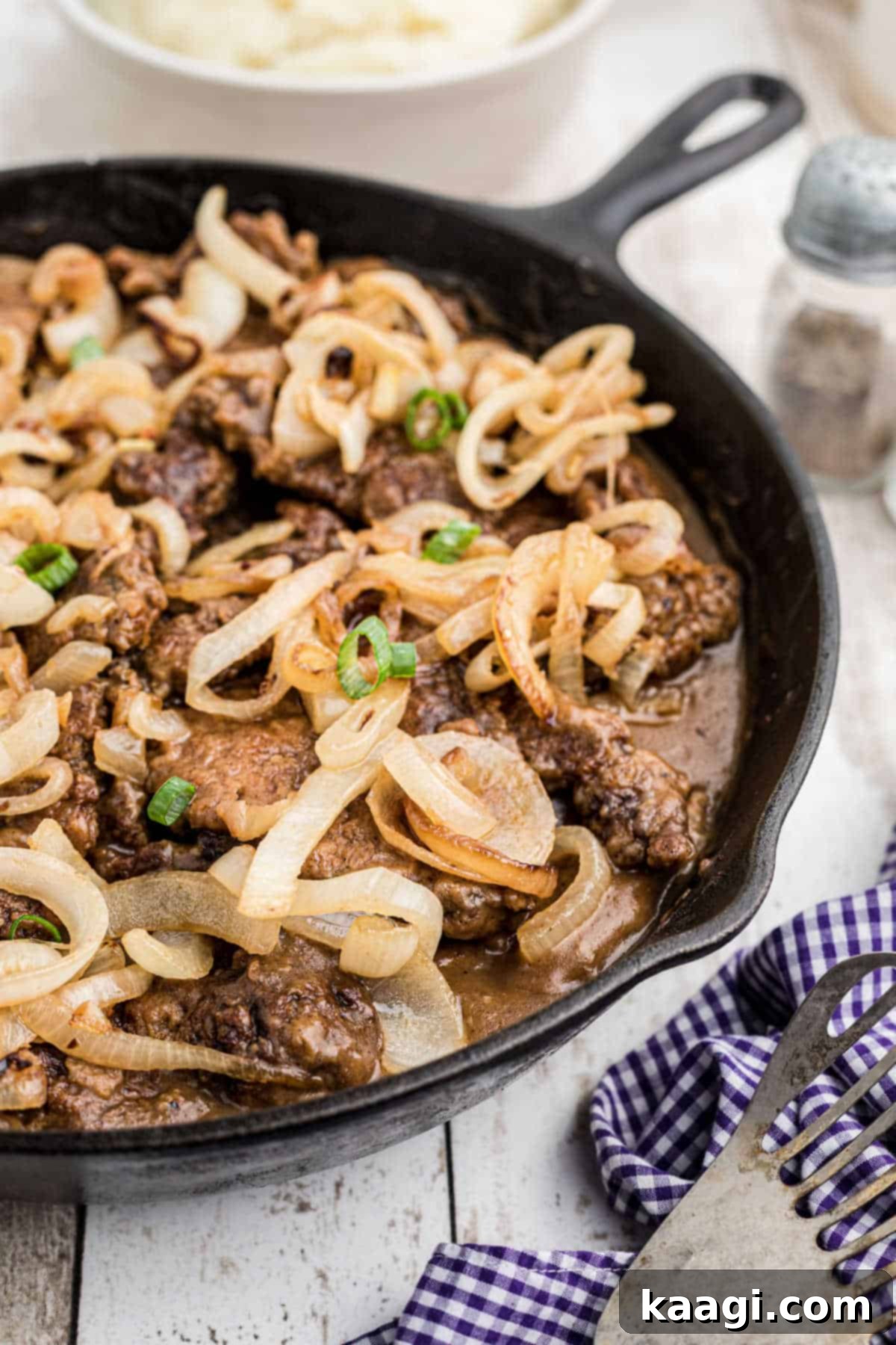 Side view of a cast iron pan with liver and onions with gravy.