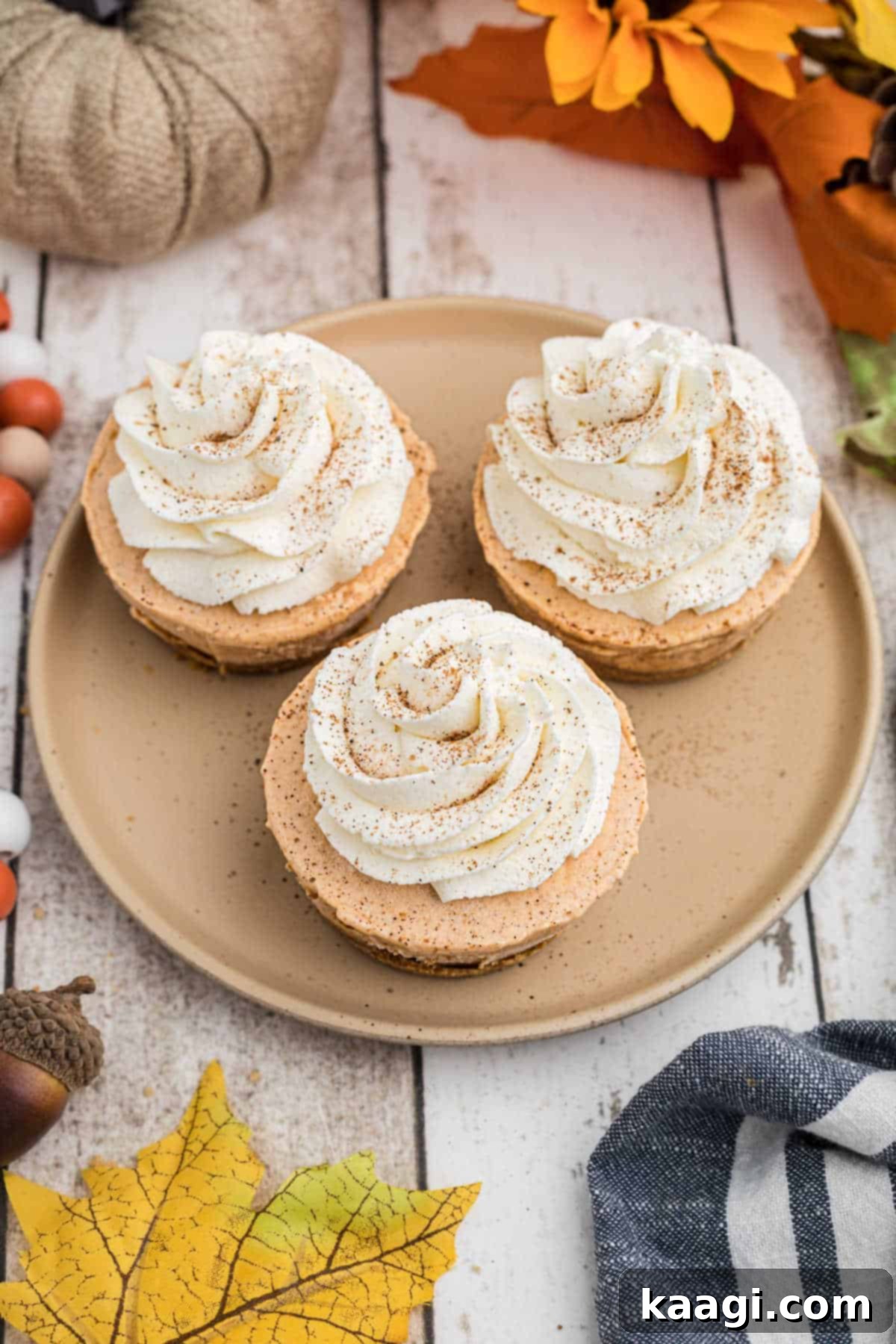 An overhead long shot of 3 mini pumpkin pies on a plate, garnished with whipped cream and a sprinkle of pumpkin pie spice.