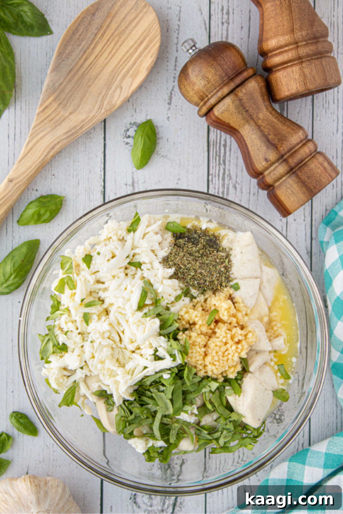 A large mixing bowl with cut refrigerated biscuits, grated cheese, minced garlic, basil, and Italian seasoning.