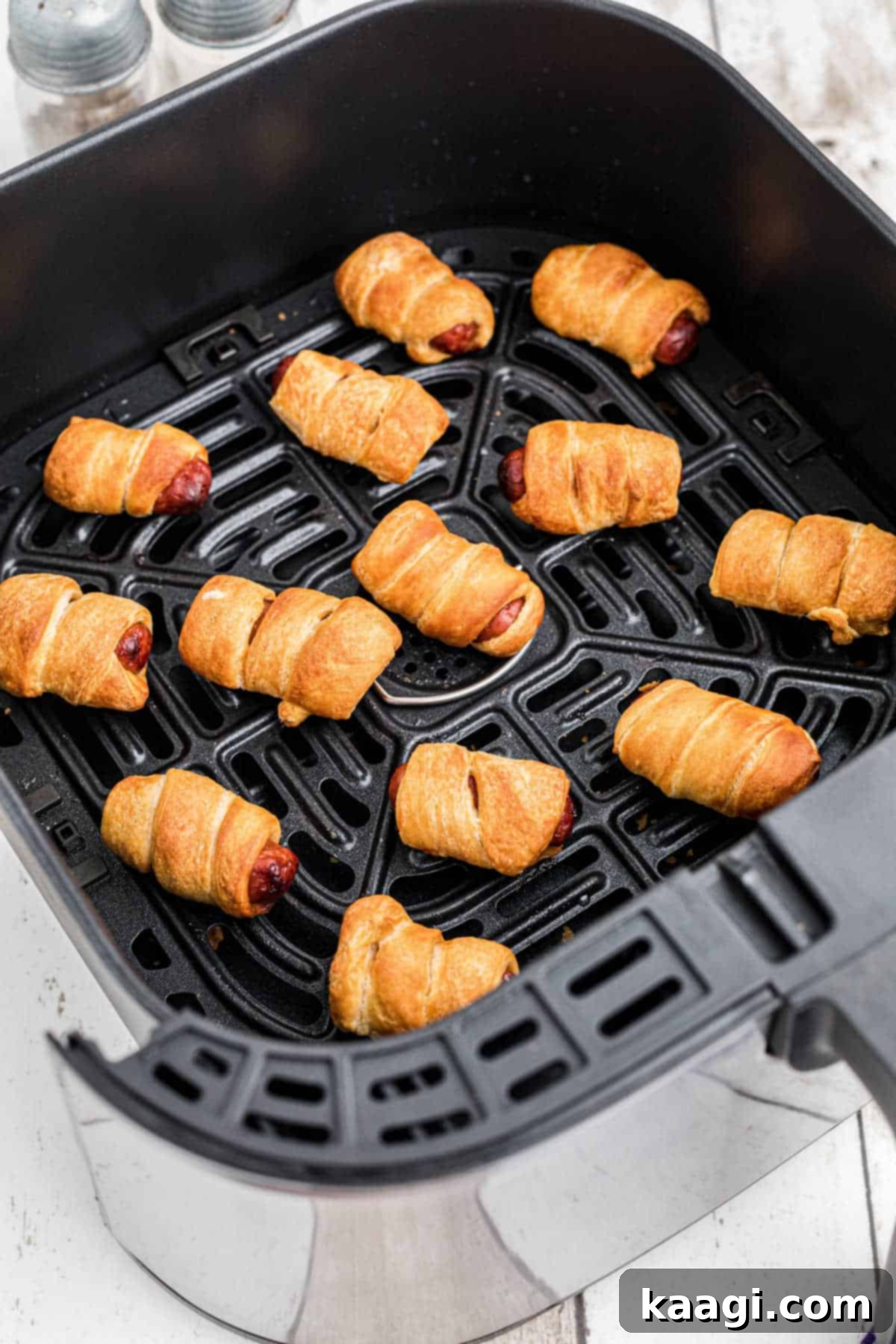 An air fryer basket full of perfectly golden-brown pigs in blankets, ready to be served.