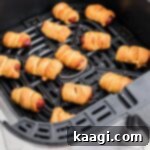 Pigs in blankets cooking in an air fryer basket.