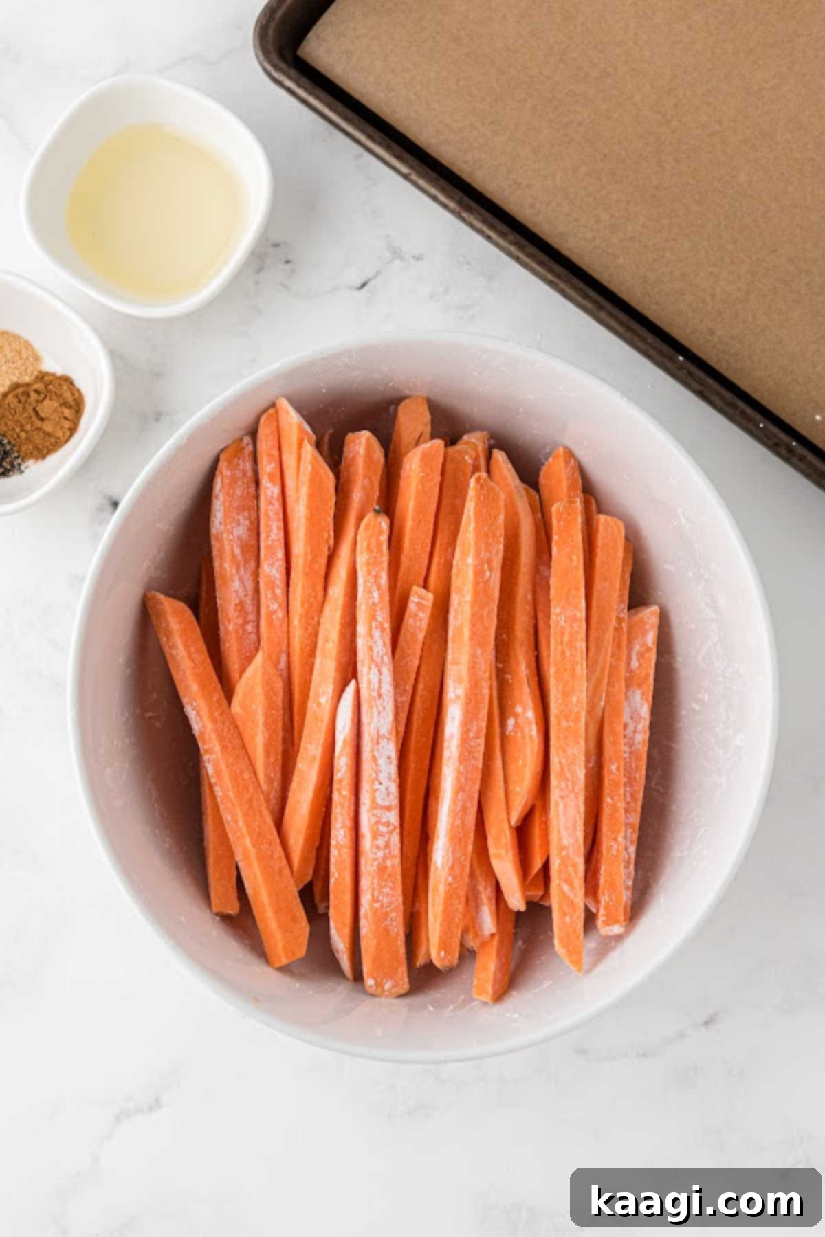 Sticks of sweet potato sticks in a bowl, with oil and ready to be coated with cornflour.