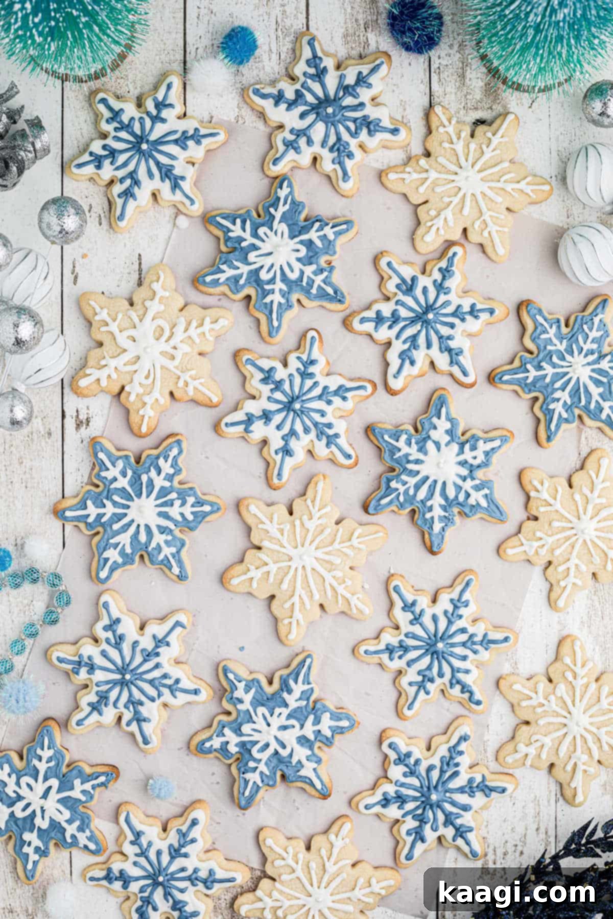 Overhead shot of a lot of snowflake cookies in white and blue, neatly arranged on a white surface.