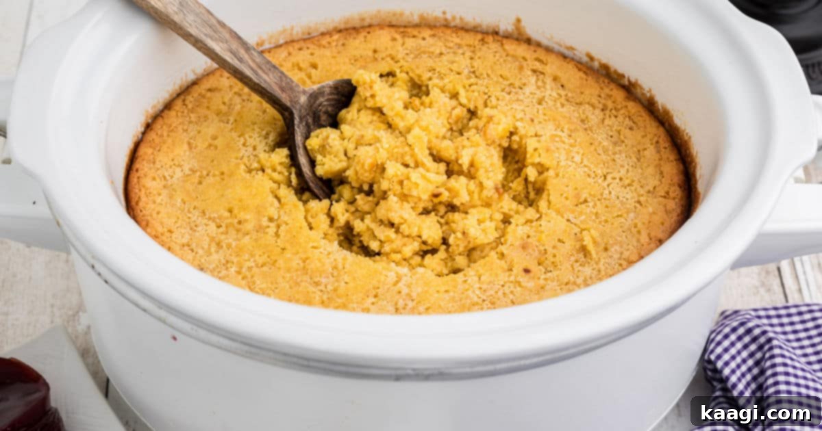 Close up of a spoon inside a Jiffy Corn Casserole in a Crock Pot, showing its moist texture.