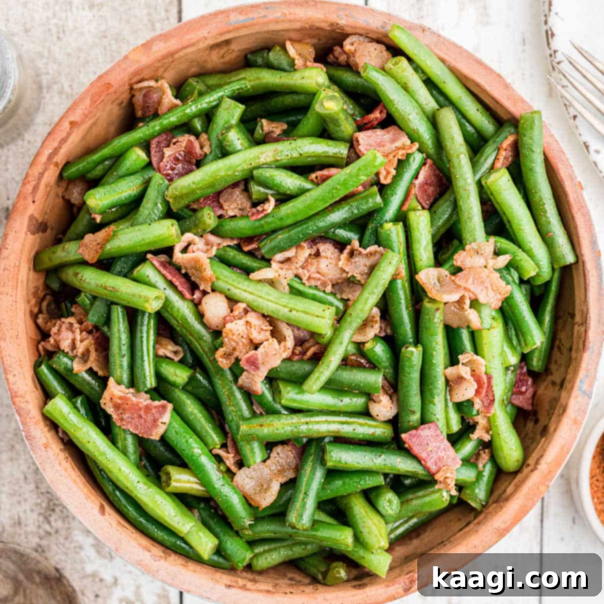 Close up of a ceramic bowl full of vibrant Cajun green beans with crispy bacon bits.