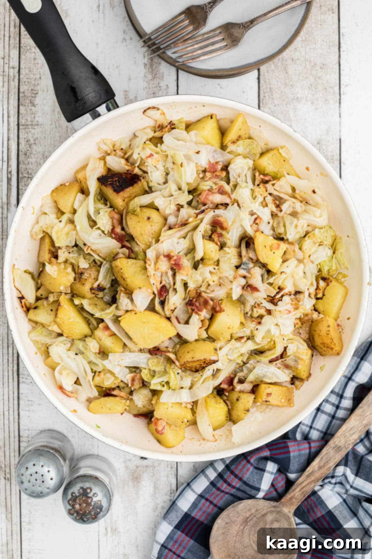 An overhead shot of a rustic cast iron skillet brimming with golden-brown fried cabbage and potatoes, garnished with fresh parsley.