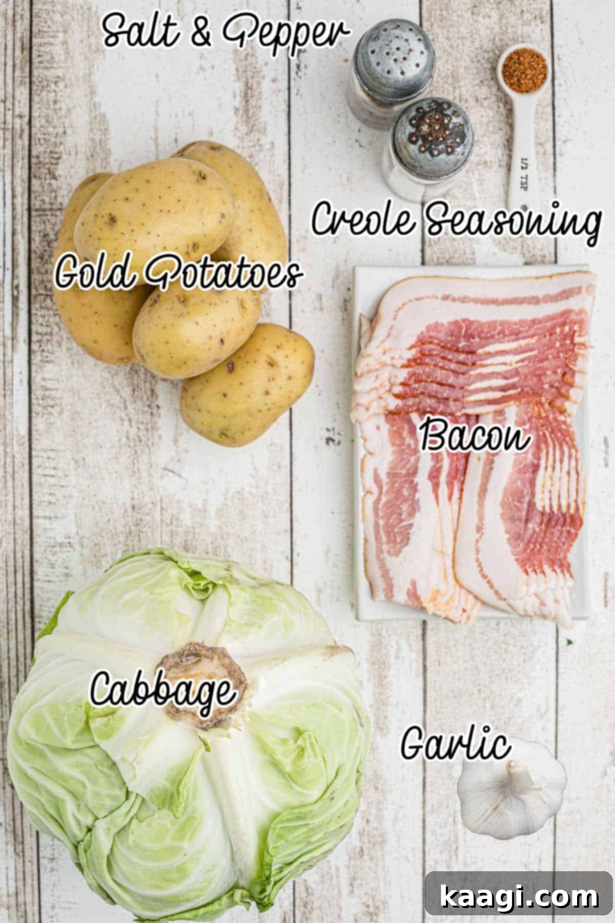 A flat lay of fresh ingredients laid out: green cabbage, yellow potatoes, strips of bacon, garlic cloves, and seasoning shakers.