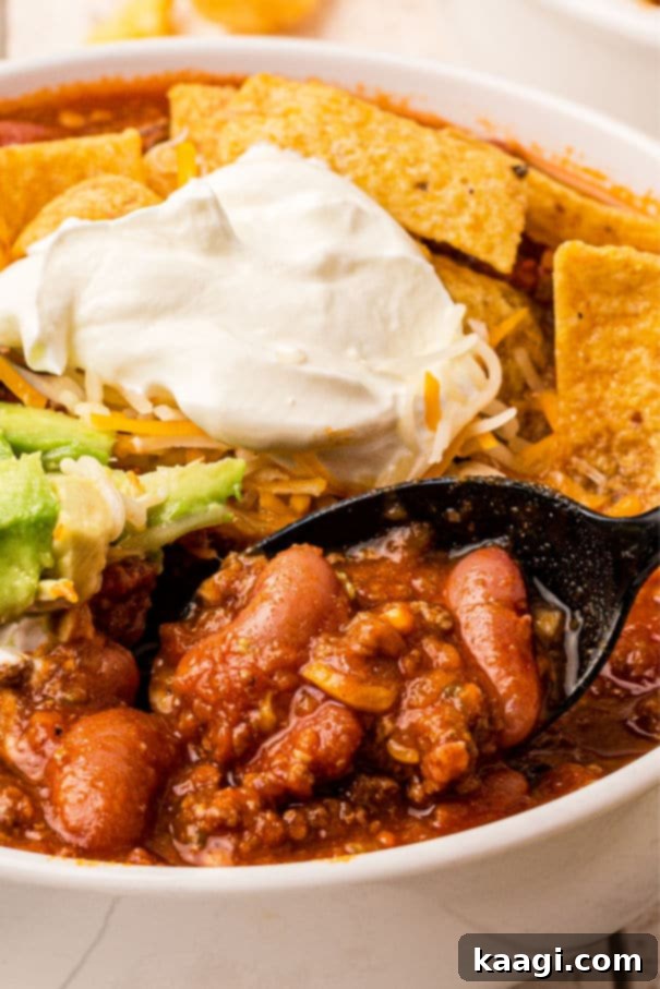 A very close up image of deer chili, with beans in it and corn chips and sour cream.