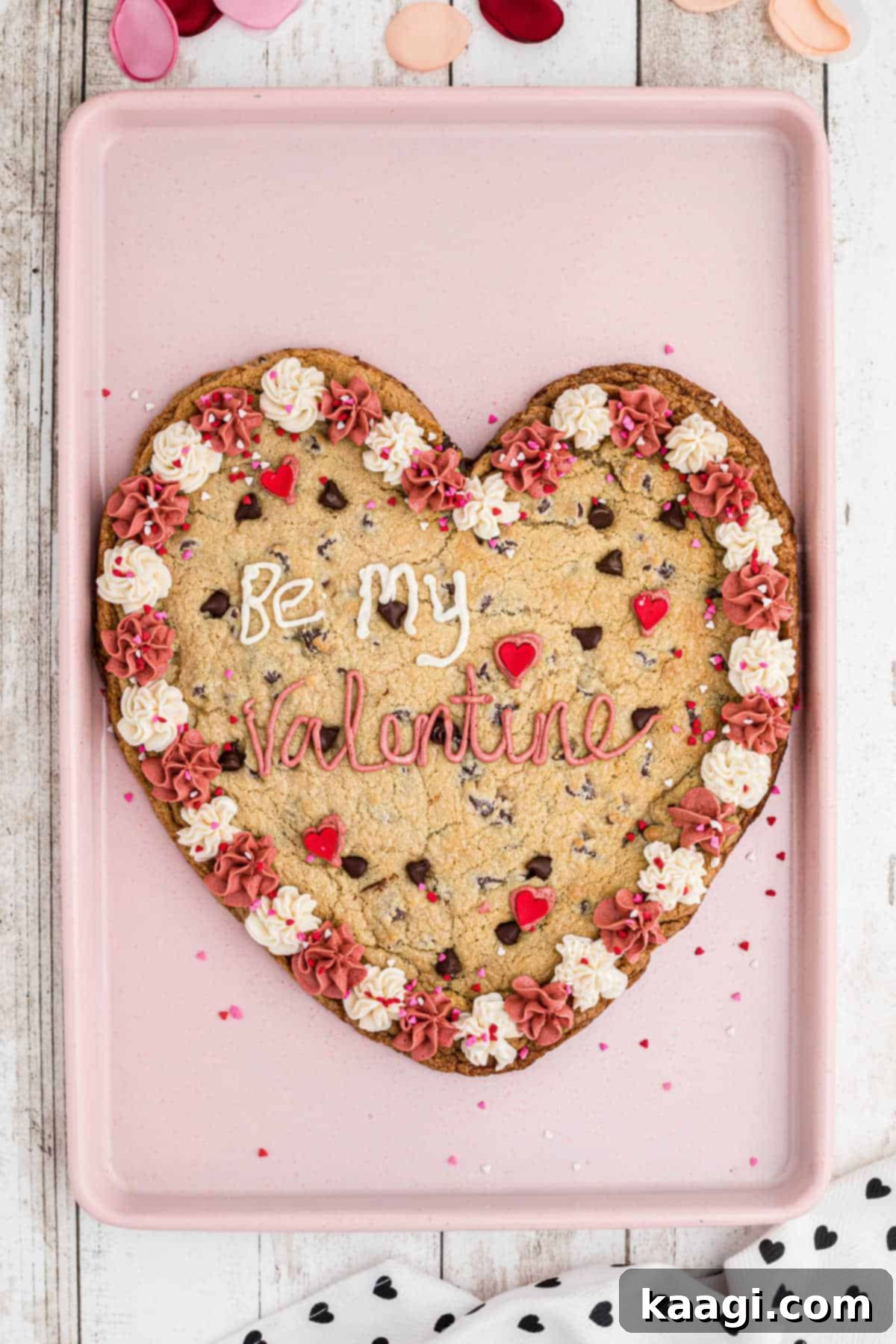 An overhead shot of a giant valentines cookie on a baking sheet, beautifully decorated with pink and white frosting.