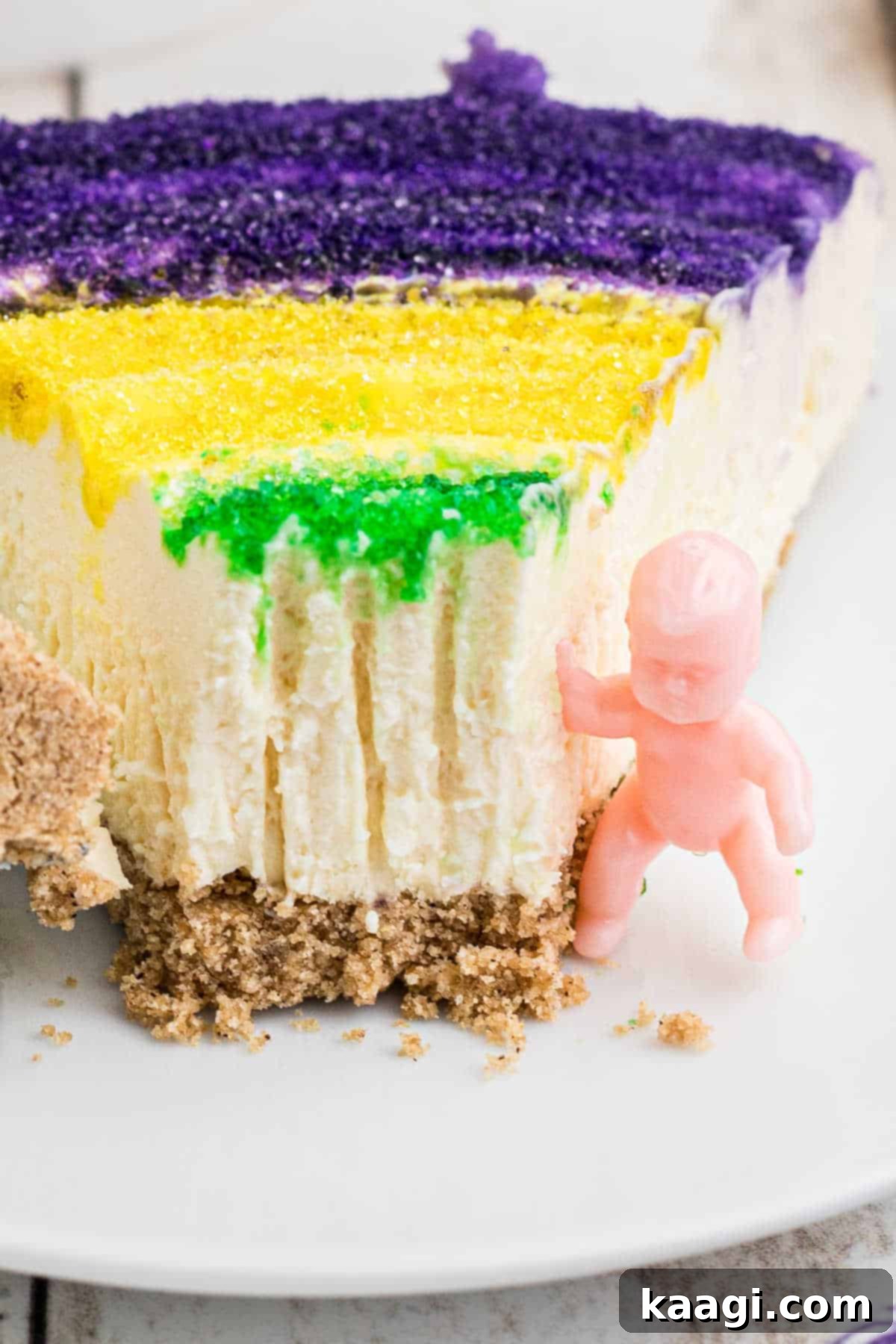 Festive Mardi Gras Cheesecake 5 Close up of a slice of mardi gras cheesecake with a king cake baby on the side.