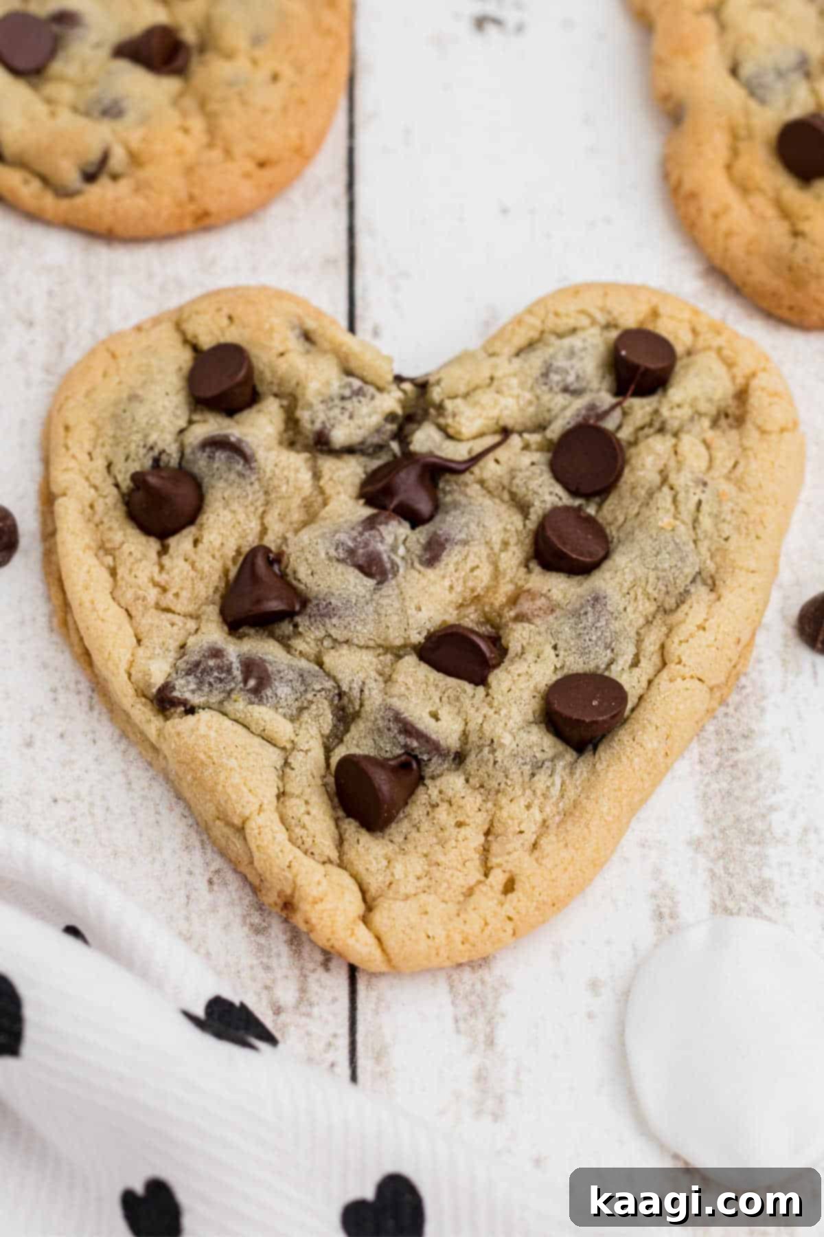 Side view of a heart shaped chocolate chip cookie, with more in the background.