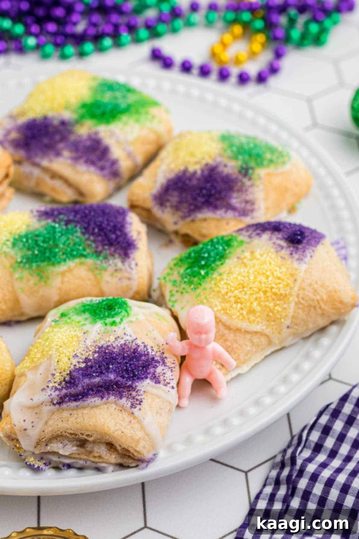 A festive plate overflowing with King Cake Bites, garnished with purple, green, and gold sanding sugars, with a traditional King Cake baby playfully placed amongst them.