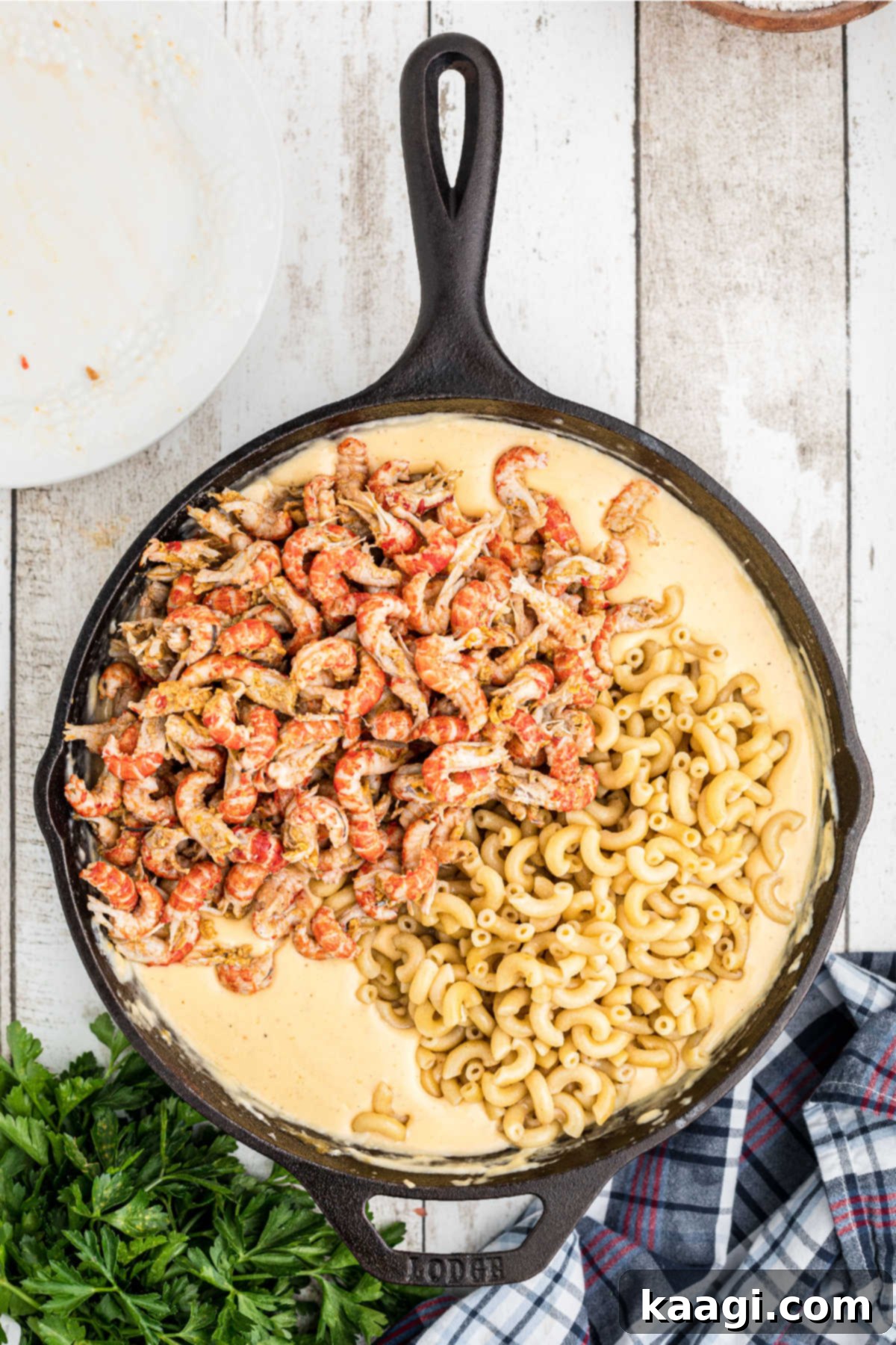 Noodles and crawfish tails added to a skillet with cheese sauce.