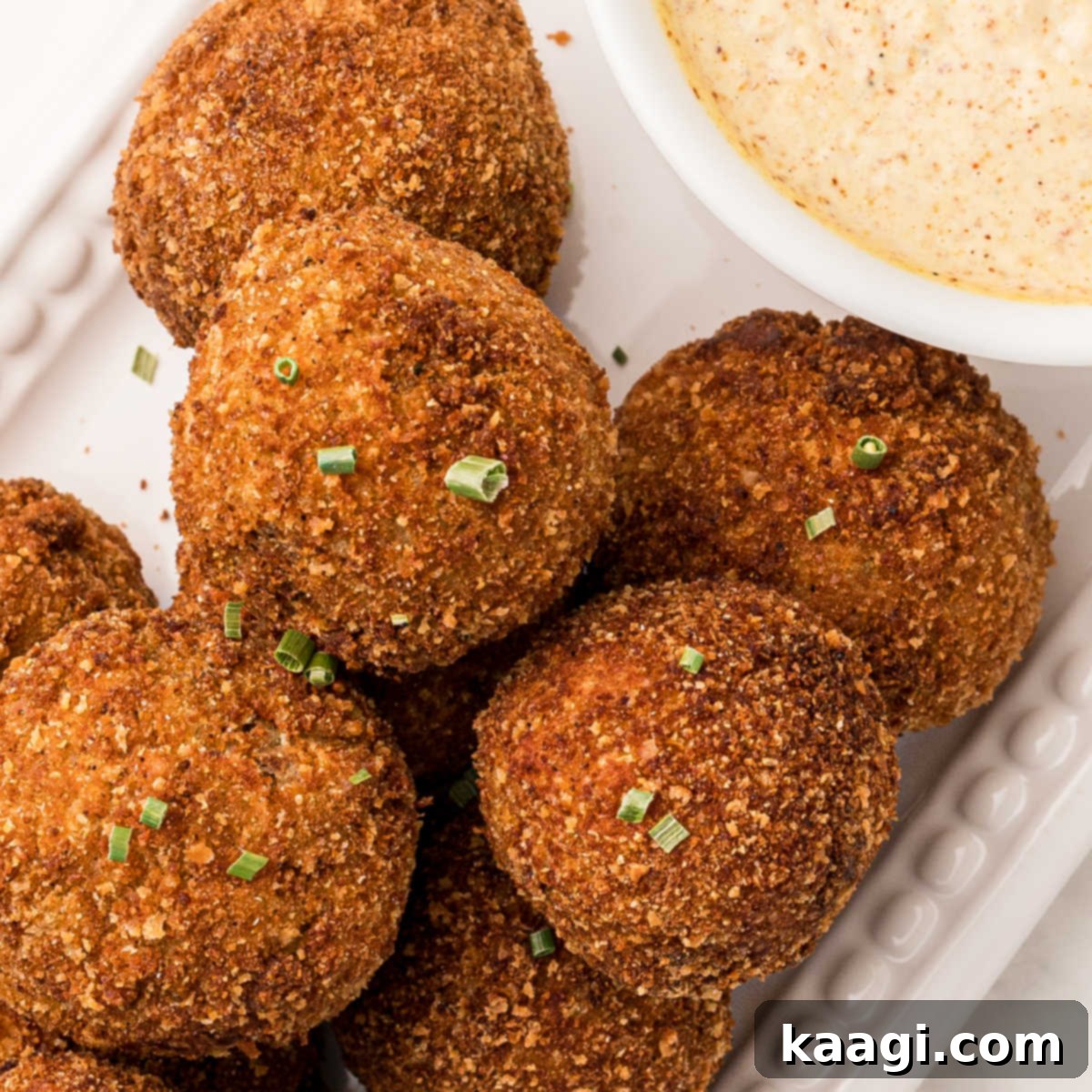 A close-up of golden brown Boudin Balls, lightly sprinkled with green onions, with a hint of dipping sauce.