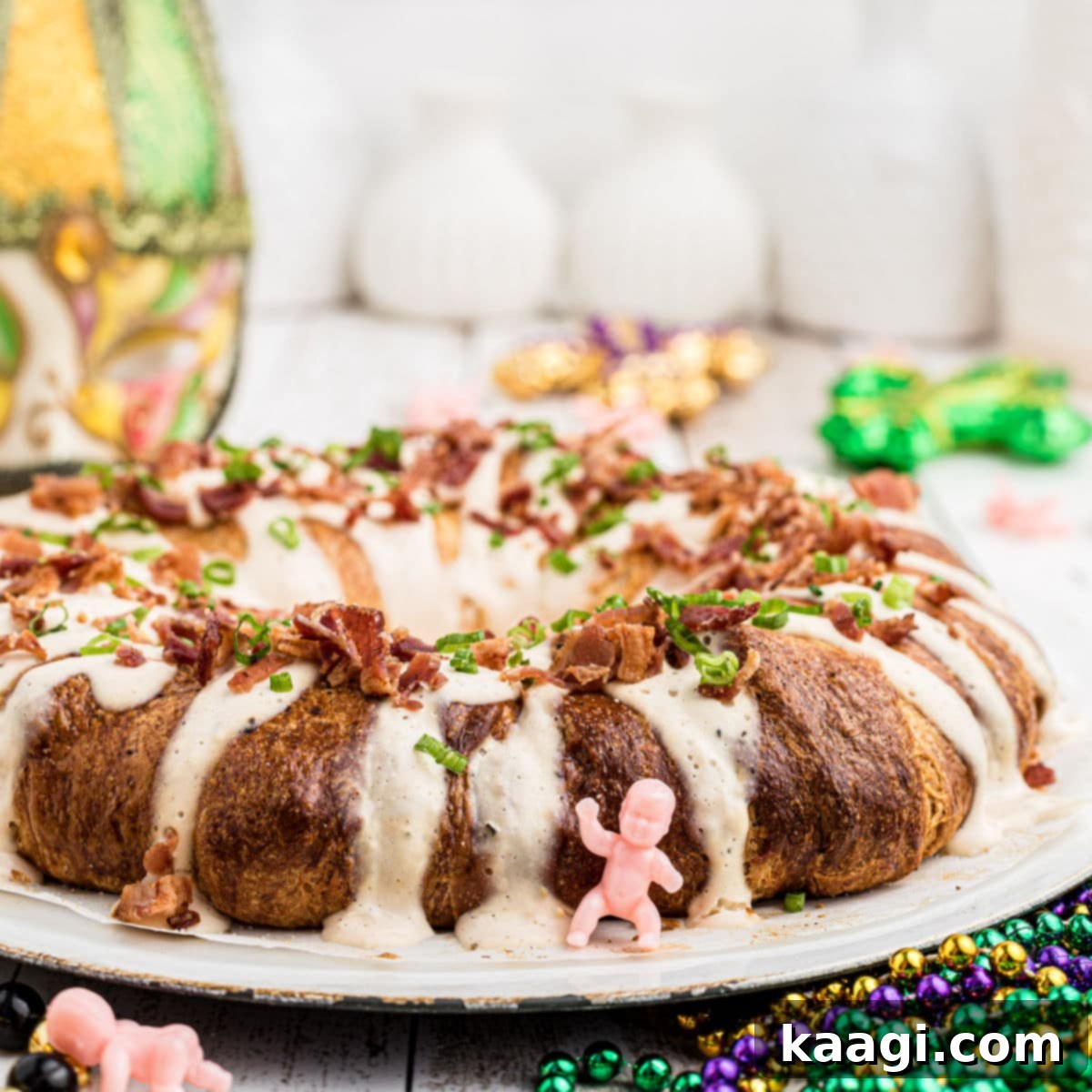 A close-up of a savory Boudin King Cake, with a king cake baby figurine and Mardi Gras decorations in the background.