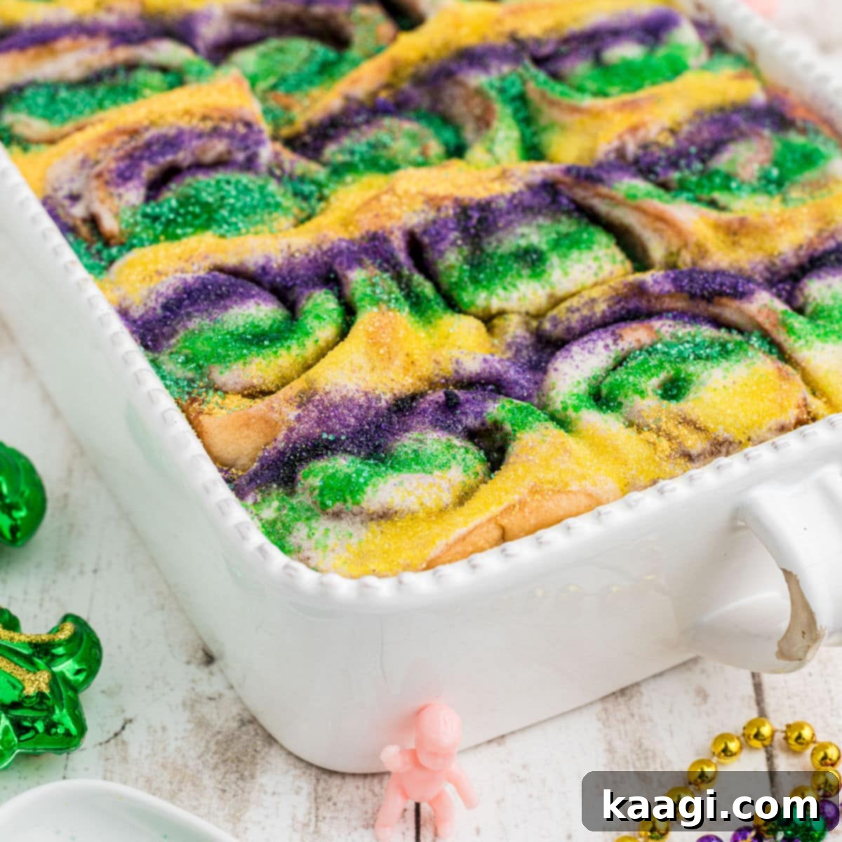 A baking dish full of fluffy King Cake Cinnamon Rolls, generously topped with icing and festive sprinkles.