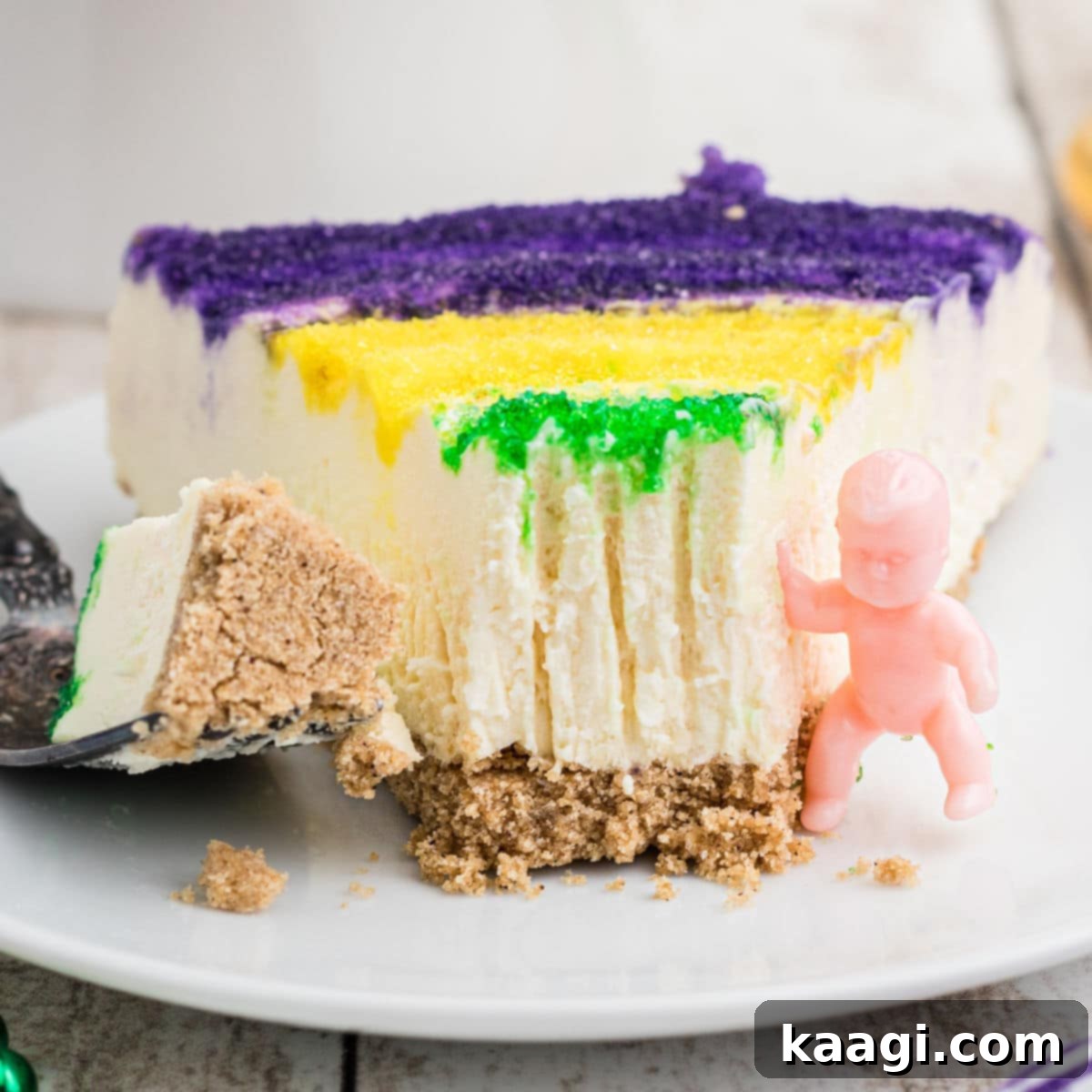 A close-up of a slice of vibrant Mardi Gras Cheesecake, garnished with festive colors and a tiny king cake baby.