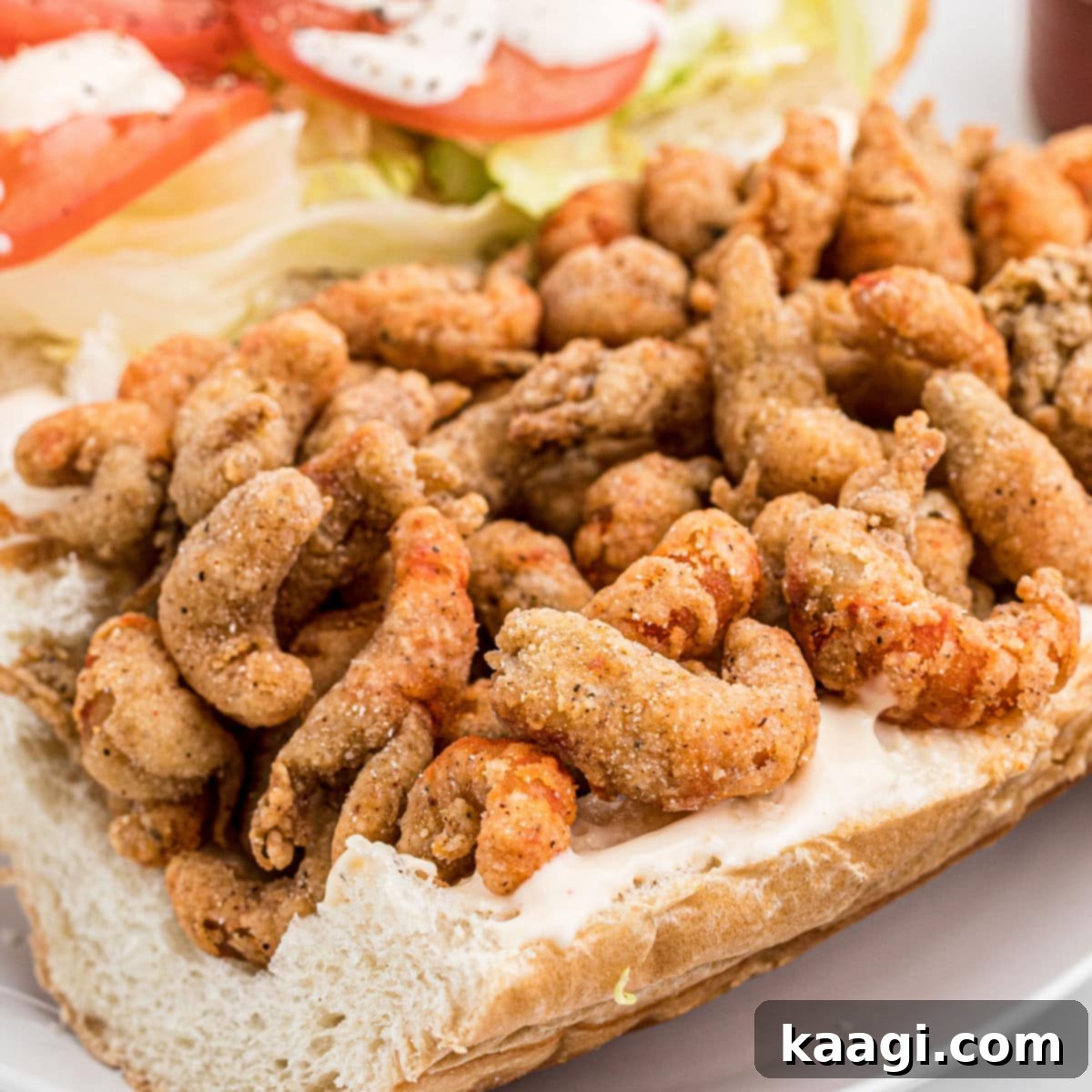 A close-up of a perfectly dressed Fried Crawfish Poboy, loaded with golden fried crawfish, lettuce, tomatoes, and mayonnaise.
