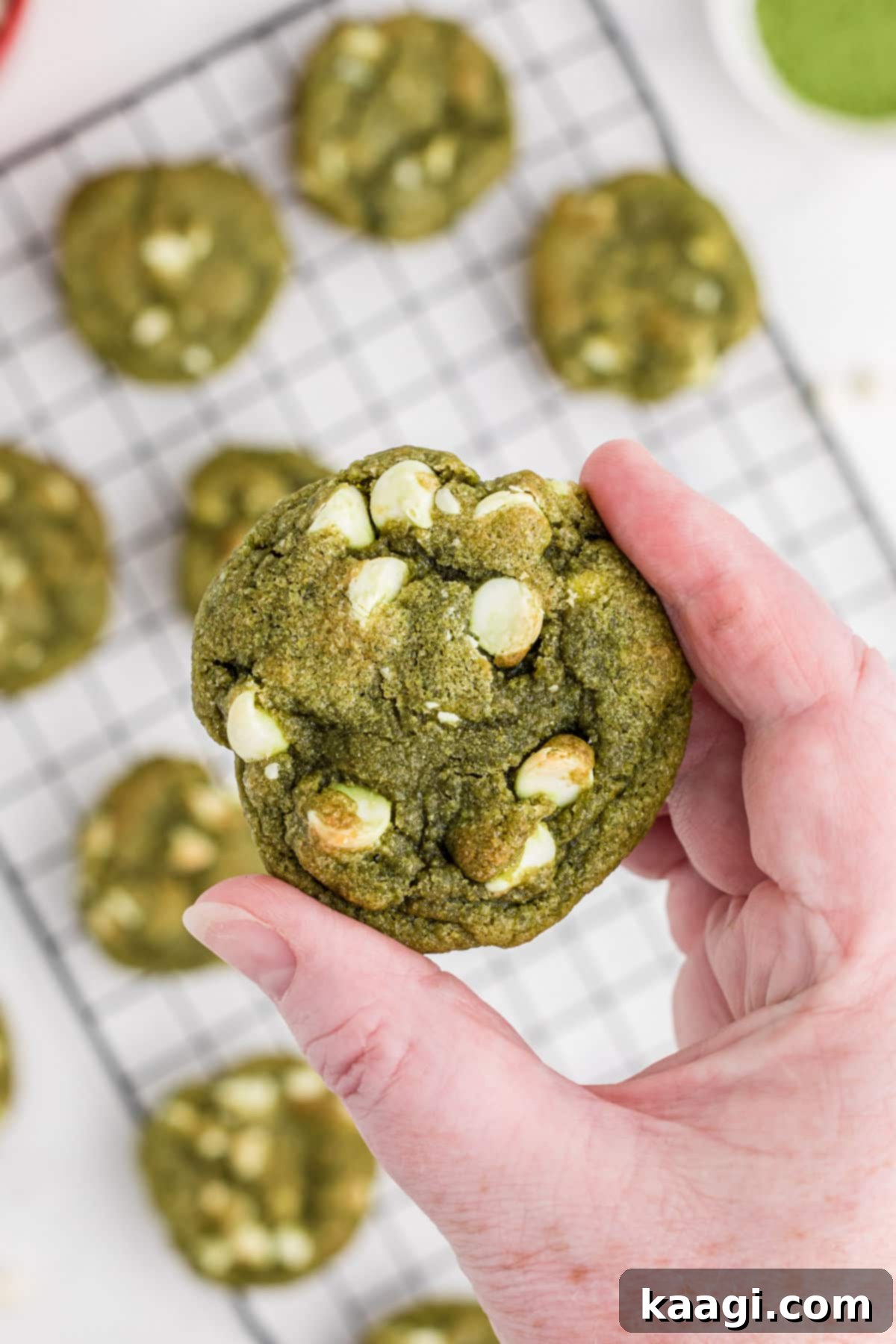 Emerald Matcha Delights 7 A hand holding up a freshly baked vibrant green matcha cookie, ready to be enjoyed.