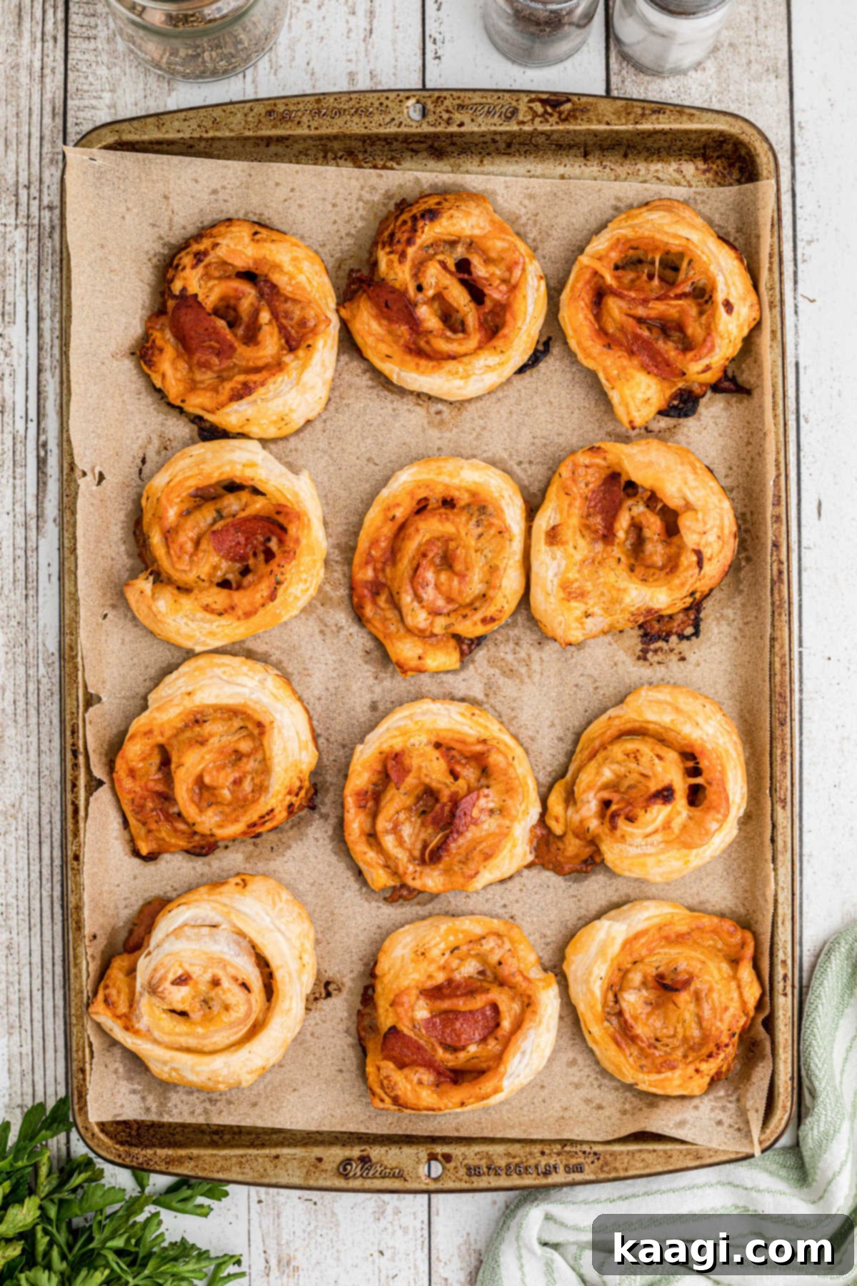 A baking sheet with parchment paper full of golden brown puff pastry pizza pinwheels, fresh from the oven.