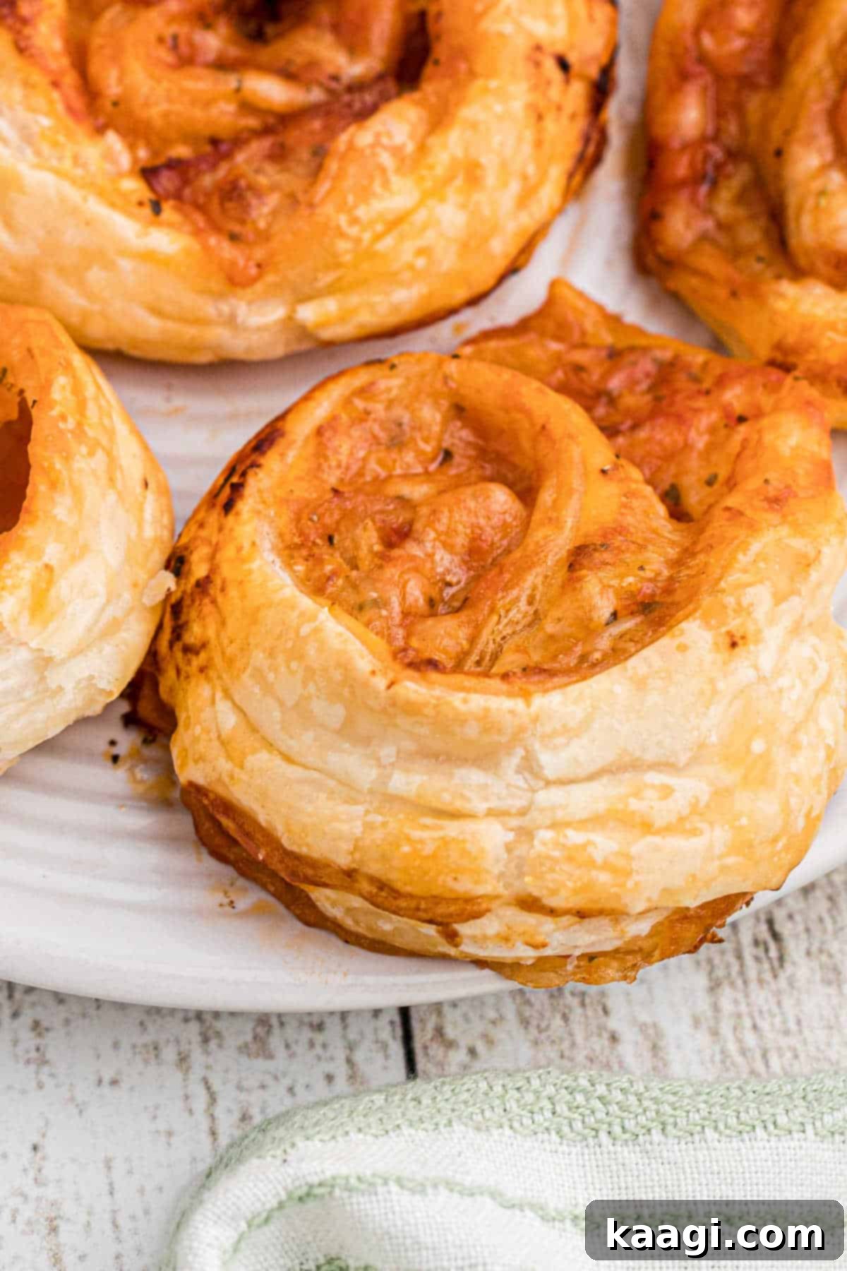 A super close-up shot of a single puff pastry pizza pinwheel, highlighting its flaky layers and melted cheese.