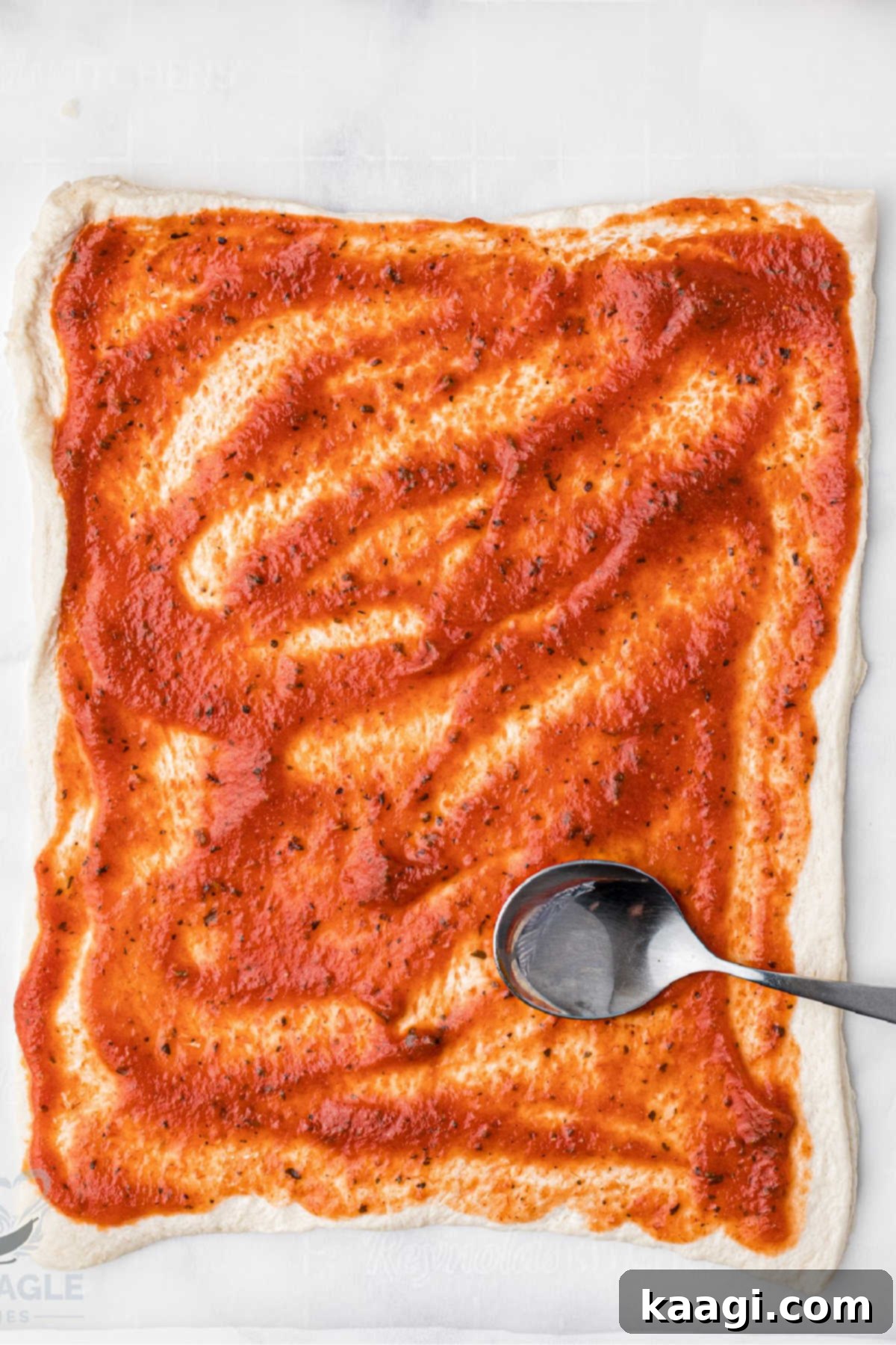 Pizza sauce evenly spread on a sheet of puff pastry.